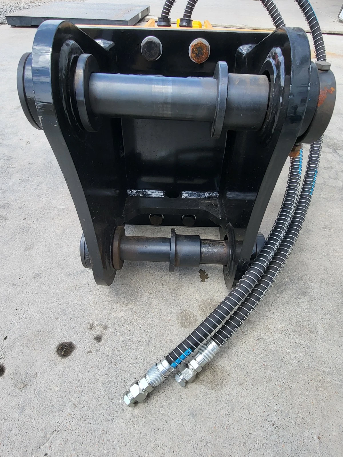 Black mounting bracket with upper and lower pins fitted, hydraulic hoses running out to the couplers