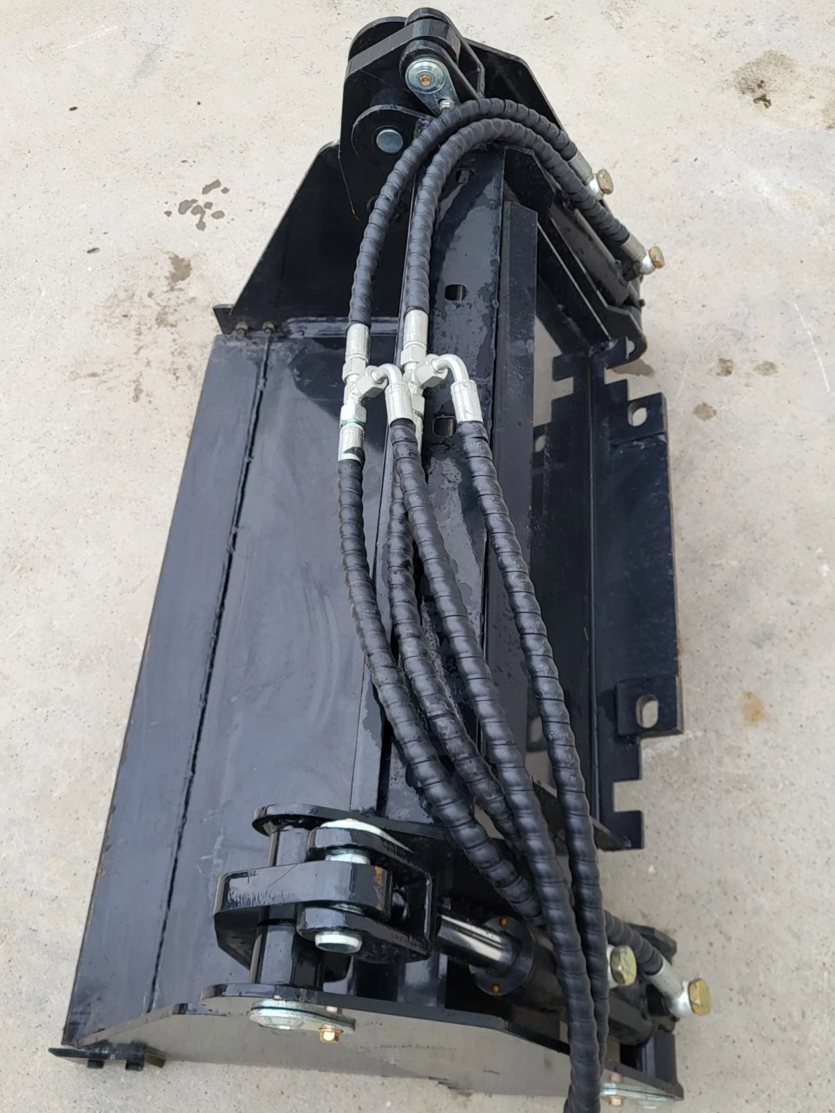 Black 4-in-1 bucket angled from above, mount frame and four braided hydraulic hoses running to the cylinders