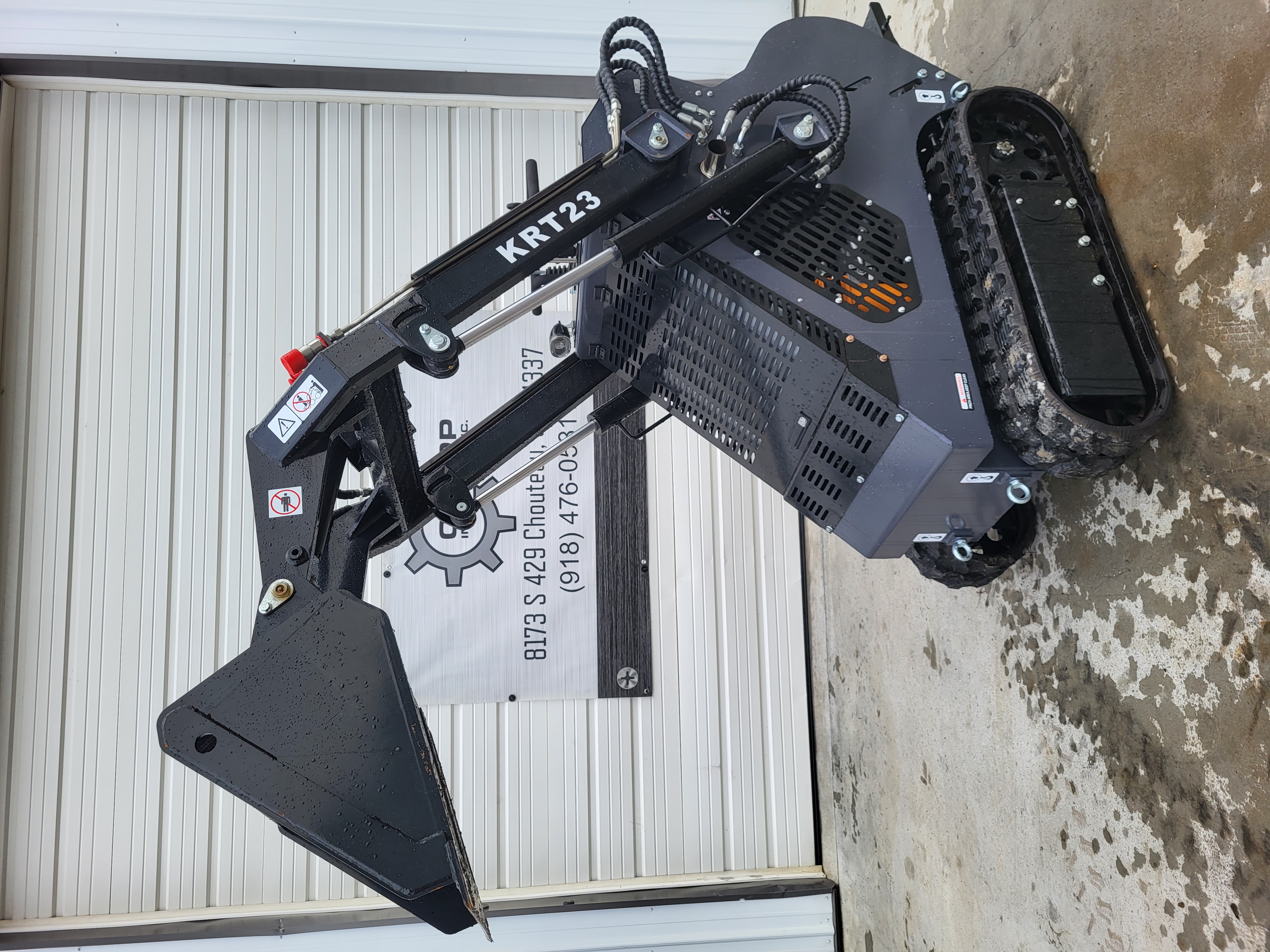KRT23 mini skid steer with the boom raised and bucket curled, tilt cylinders and hoses along the black arms