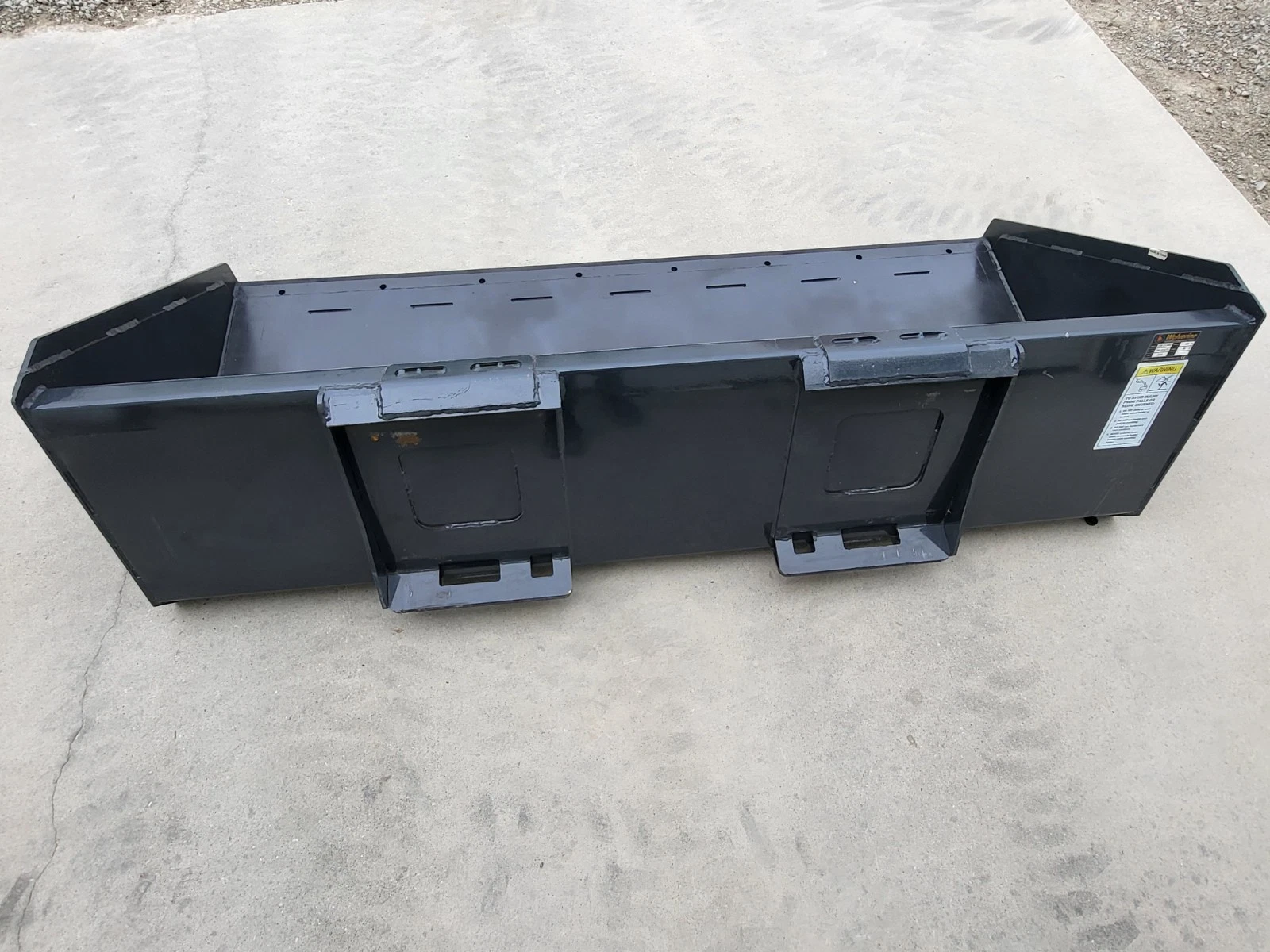 Wolverine bucket from behind: two quick-attach mounting brackets with latch slots and a warning decal