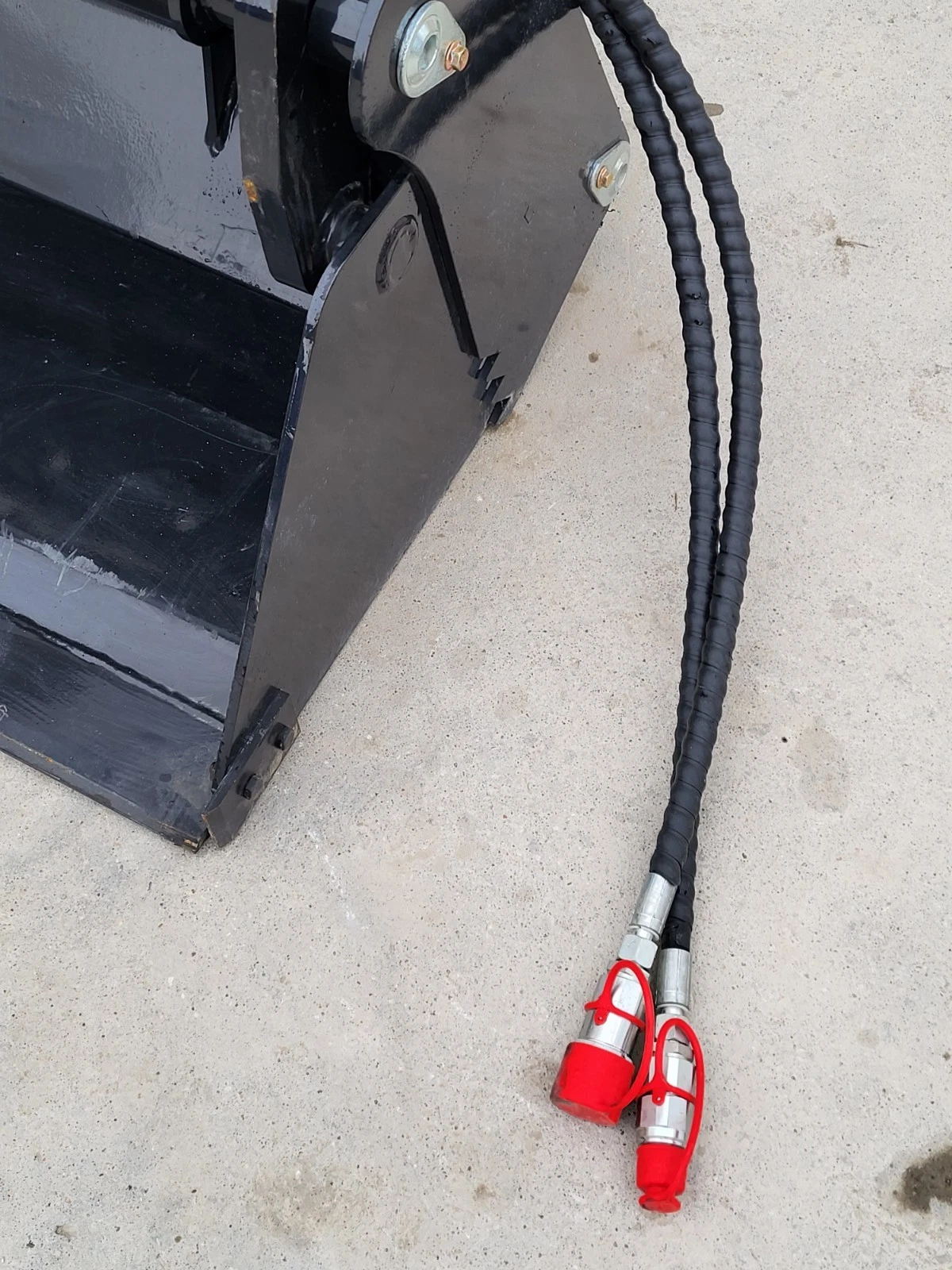 Bucket's side plate and jaw edge, two braided hoses running out to red-capped quick couplers