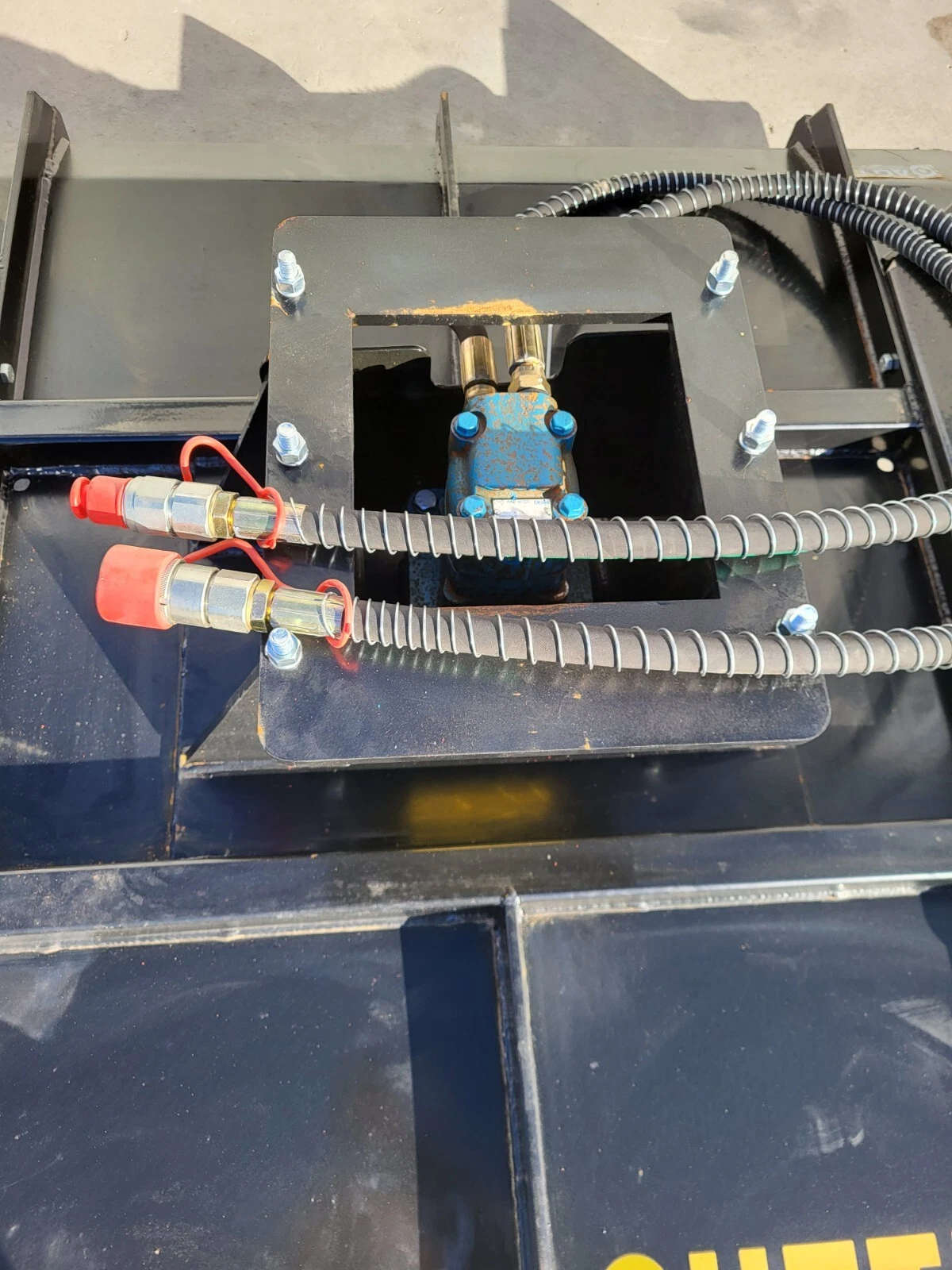 Blue hydraulic valve under the deck's access plate, red-capped quick-connect couplers and sheathed hoses