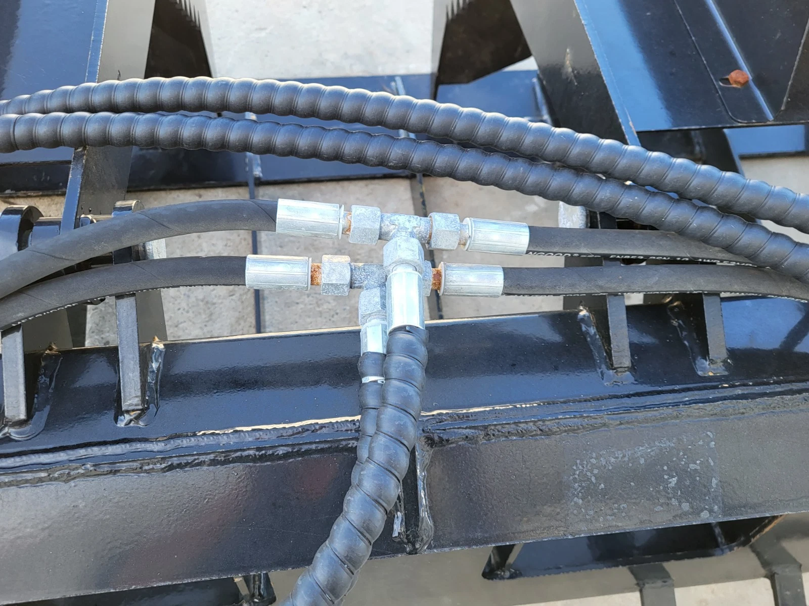Hydraulic tee fitting splitting the hose run across the root grapple's tine frame