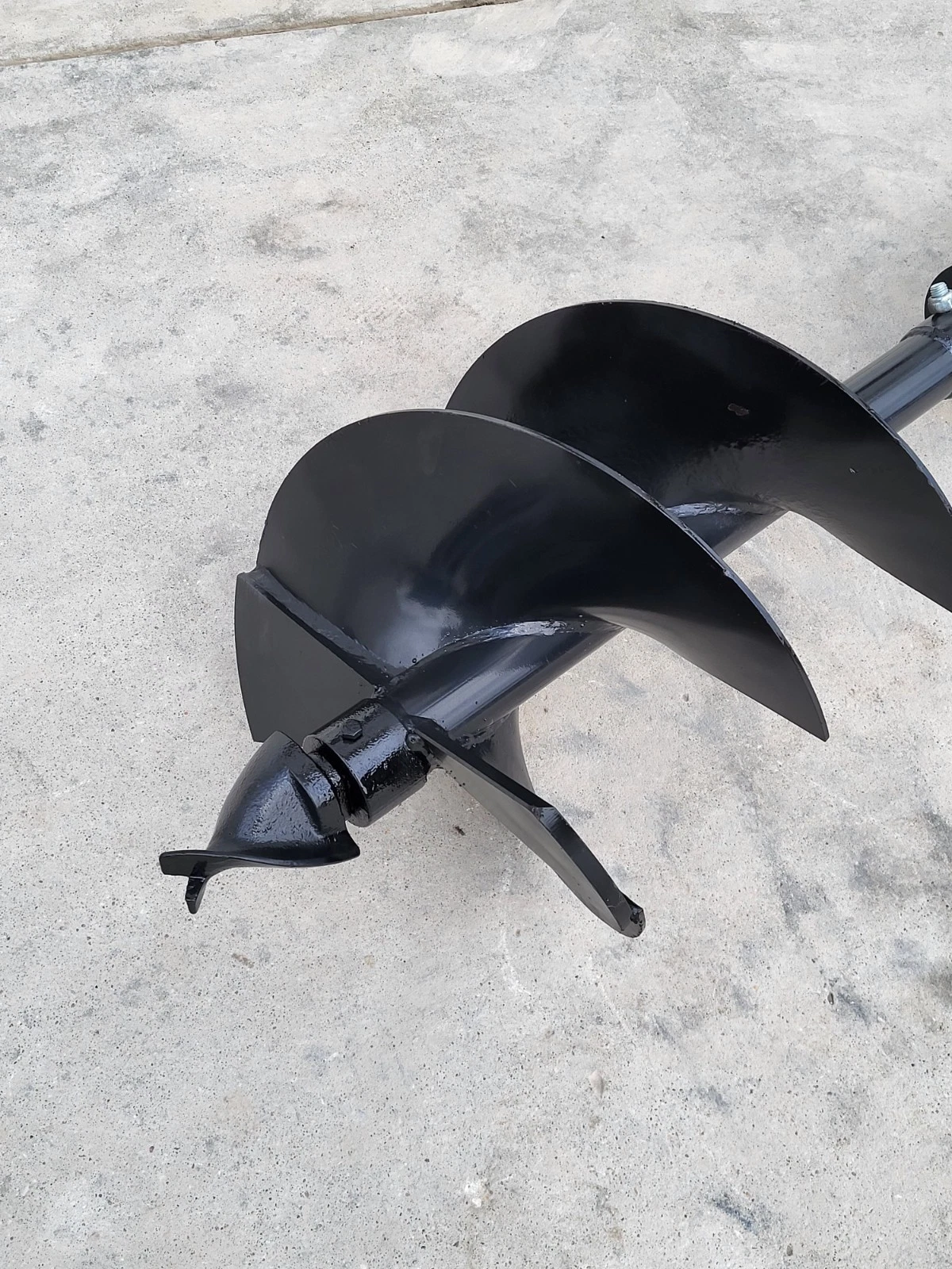 Auger bit head close-up: two black steel flights, cast pilot point and twin cutting teeth