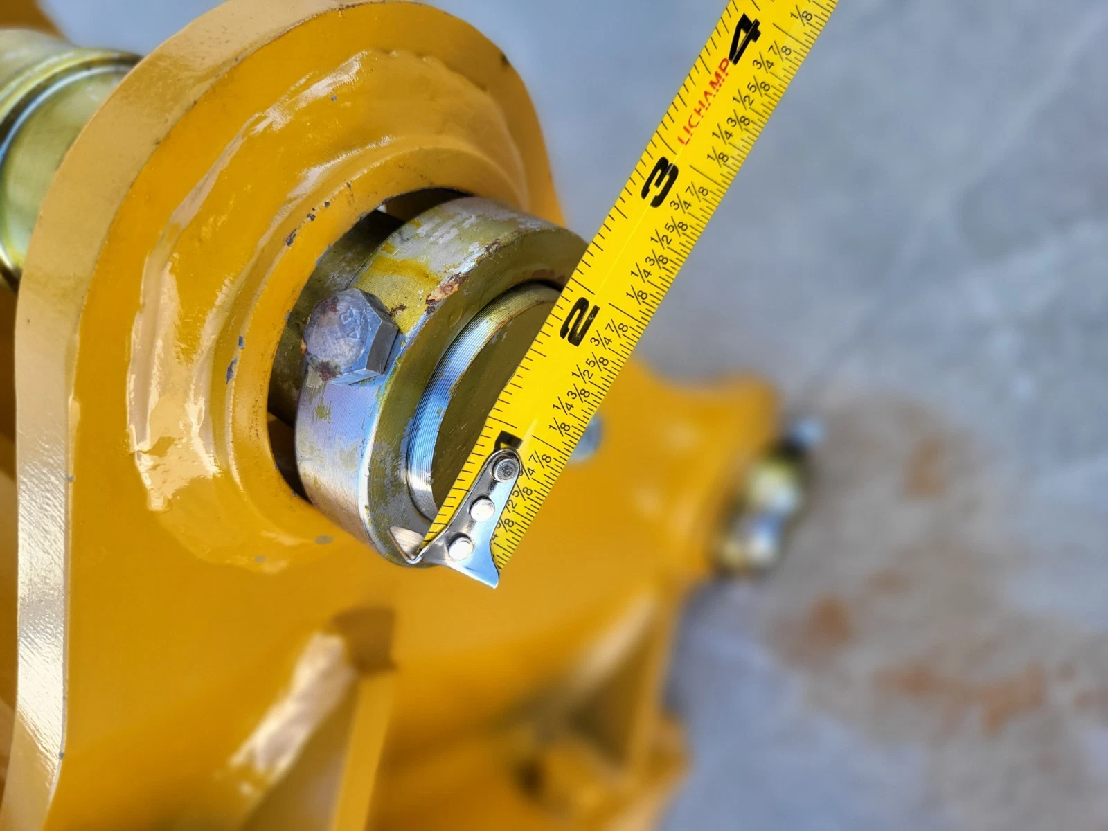 Pin, retaining bolt and bushing in the yellow mounting bracket, tape measure alongside reading about 3 inches