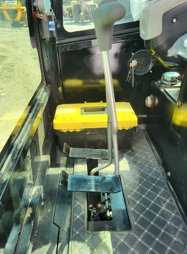 Mini excavator cab interior: travel lever and foot pedals, yellow tool box on the floor, key in the ignition