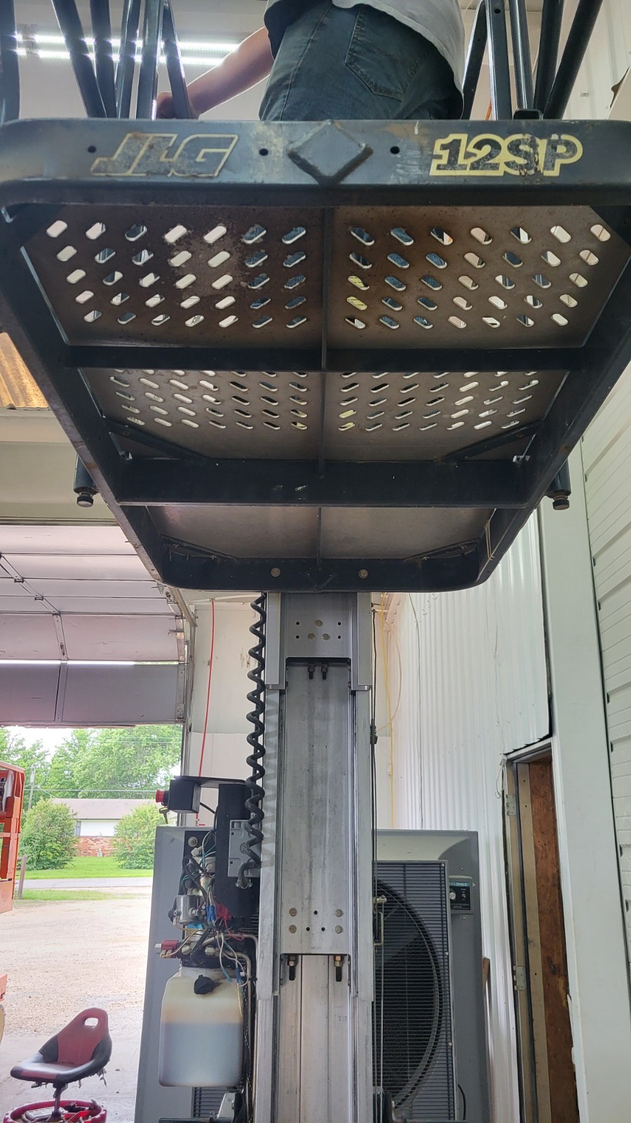 Underside of the JLG 12SP platform: JLG 12SP badge and perforated steel deck with the mast below