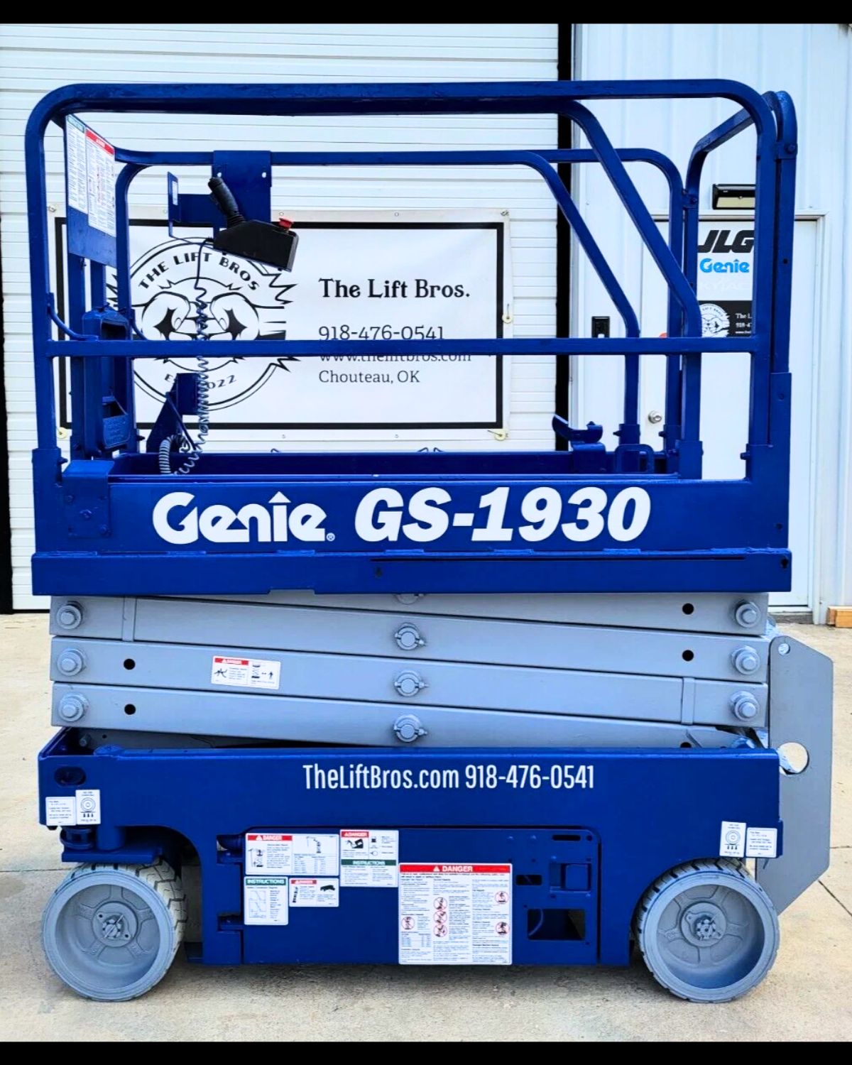 Genie GS-1930 scissor lift in blue, platform lowered with guardrails up, hand controller on the rail, solid tires