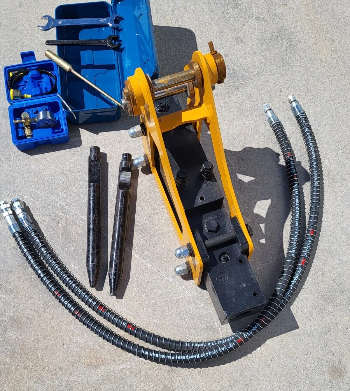 Yellow hydraulic breaker with two chisels, hoses, tool box and nitrogen charging kit laid out