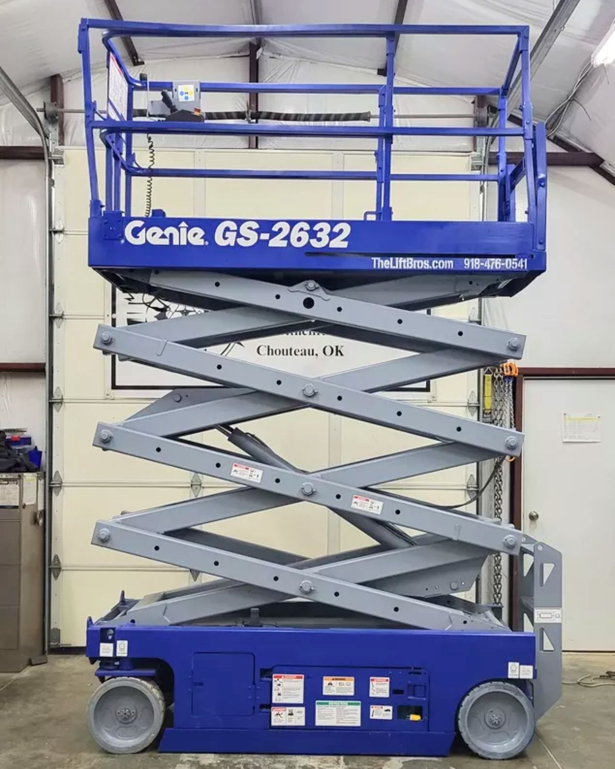 Blue Genie GS-2632 scissor lift partly raised on its scissor stack, guardrails and platform controls, non-marking wheels