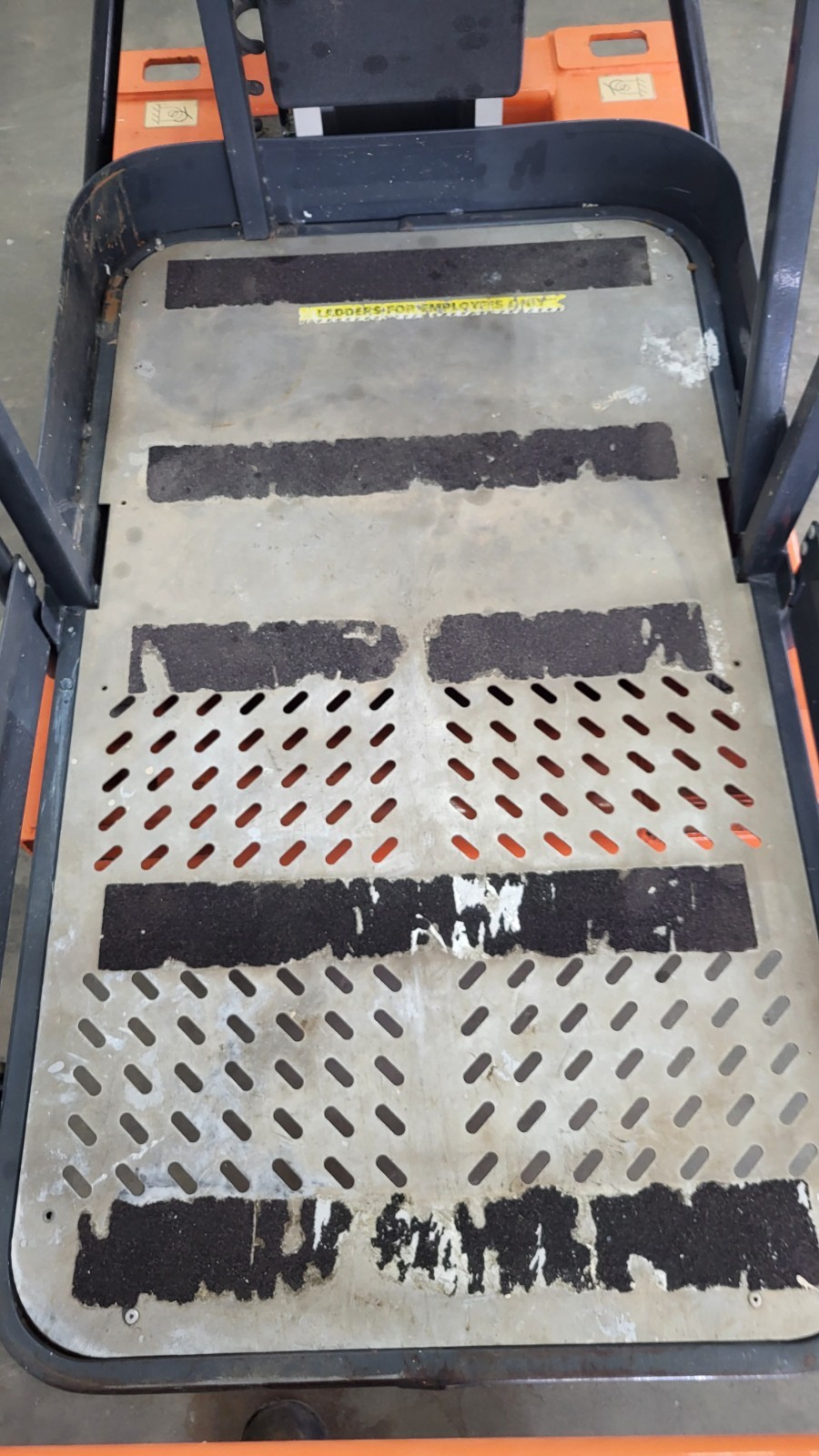 JLG 12SP platform deck: perforated steel floor with worn black anti-slip strips