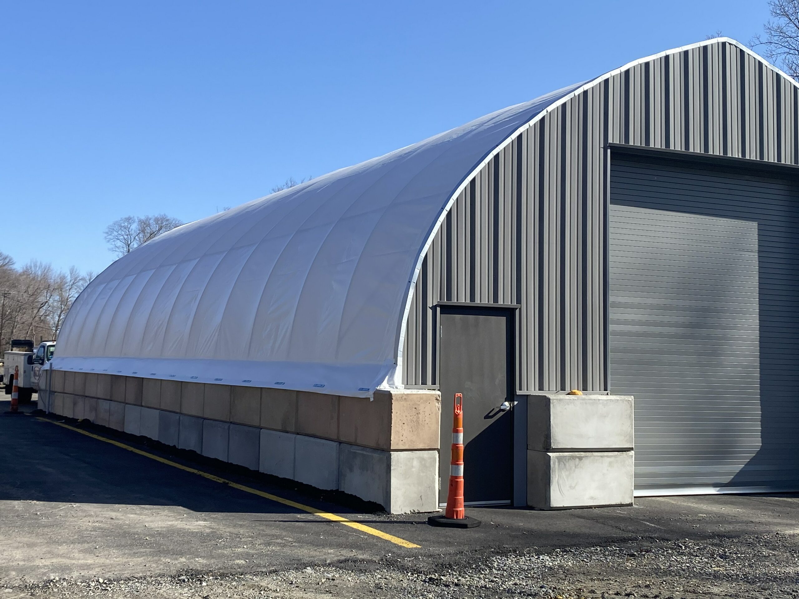 White PVC fabric building curving off the end of a steel shop, cover anchored on stacked concrete block walls