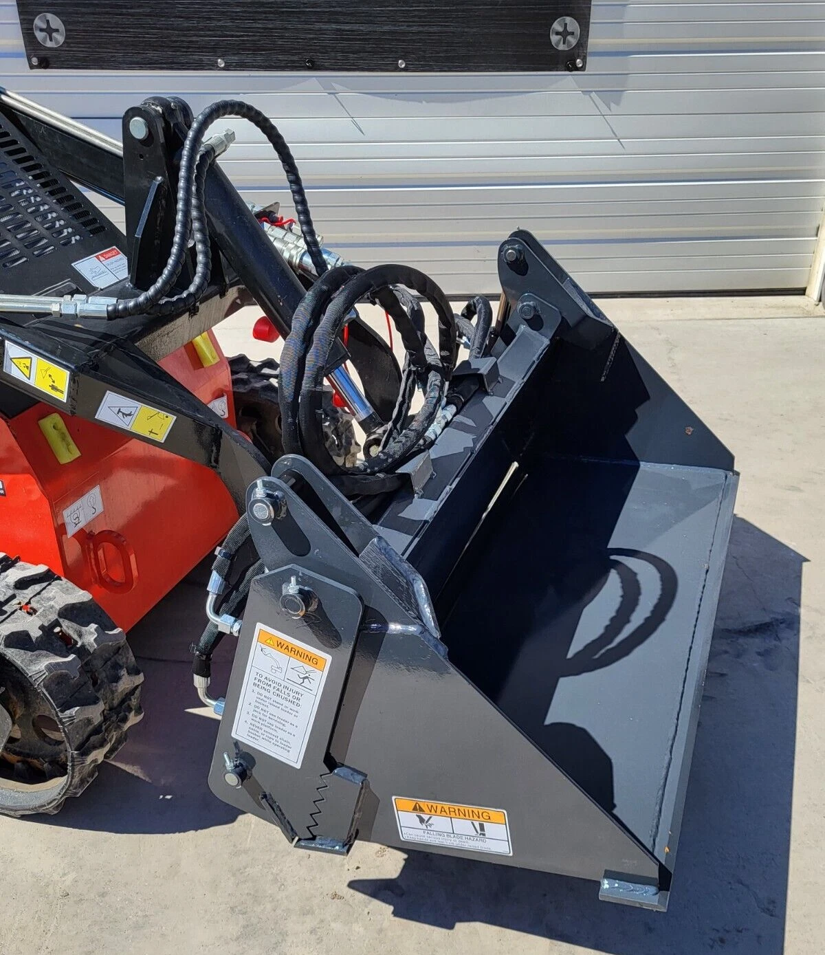 Gray 4-in-1 bucket mounted on an orange mini skid steer, serrated clamshell jaw, hoses and warning decals