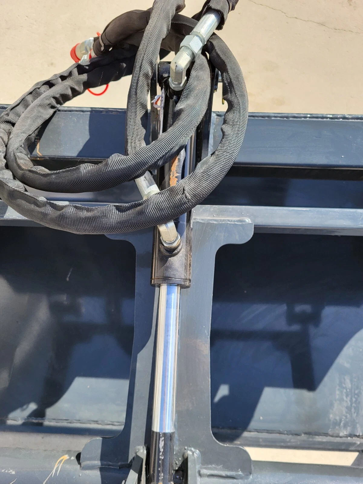 Hydraulic cylinder rod and sleeved hoses on the grapple bucket's gray frame