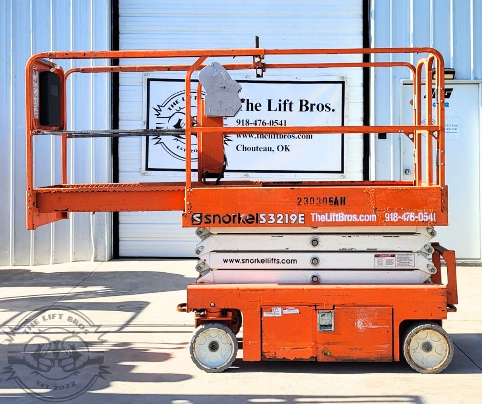 Orange Snorkel S3219E scissor lift, fully lowered, guardrails around the platform and the slide-out extension deck