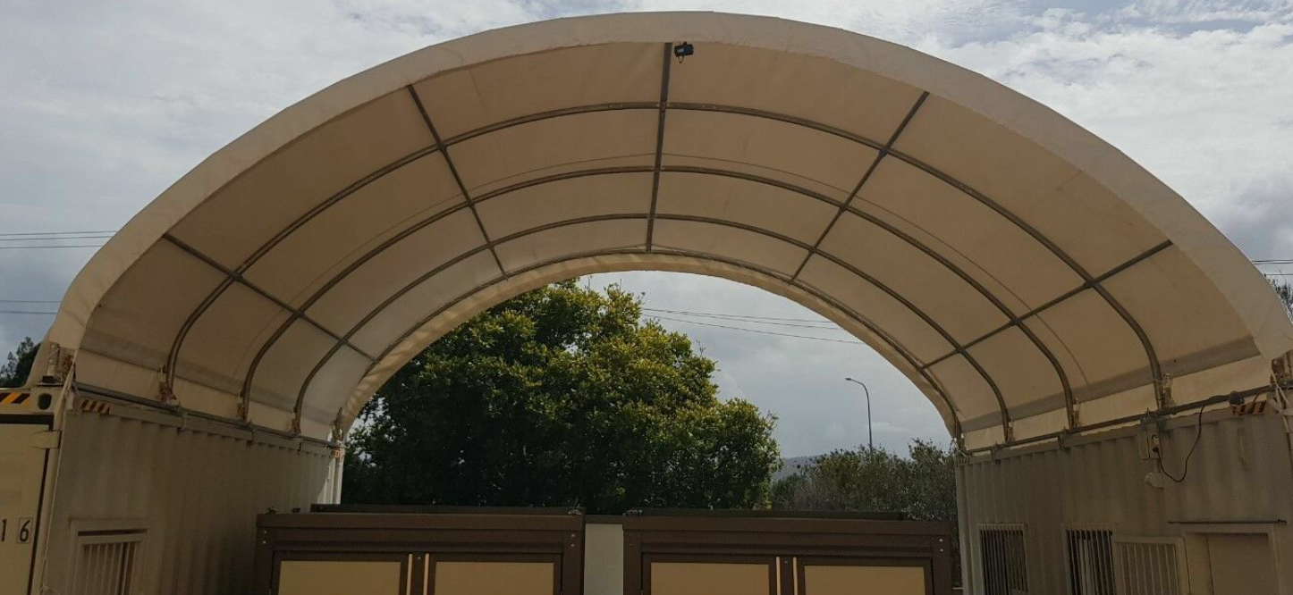 Container shelter's arched fabric roof on galvanized purlins, open at both ends between two containers