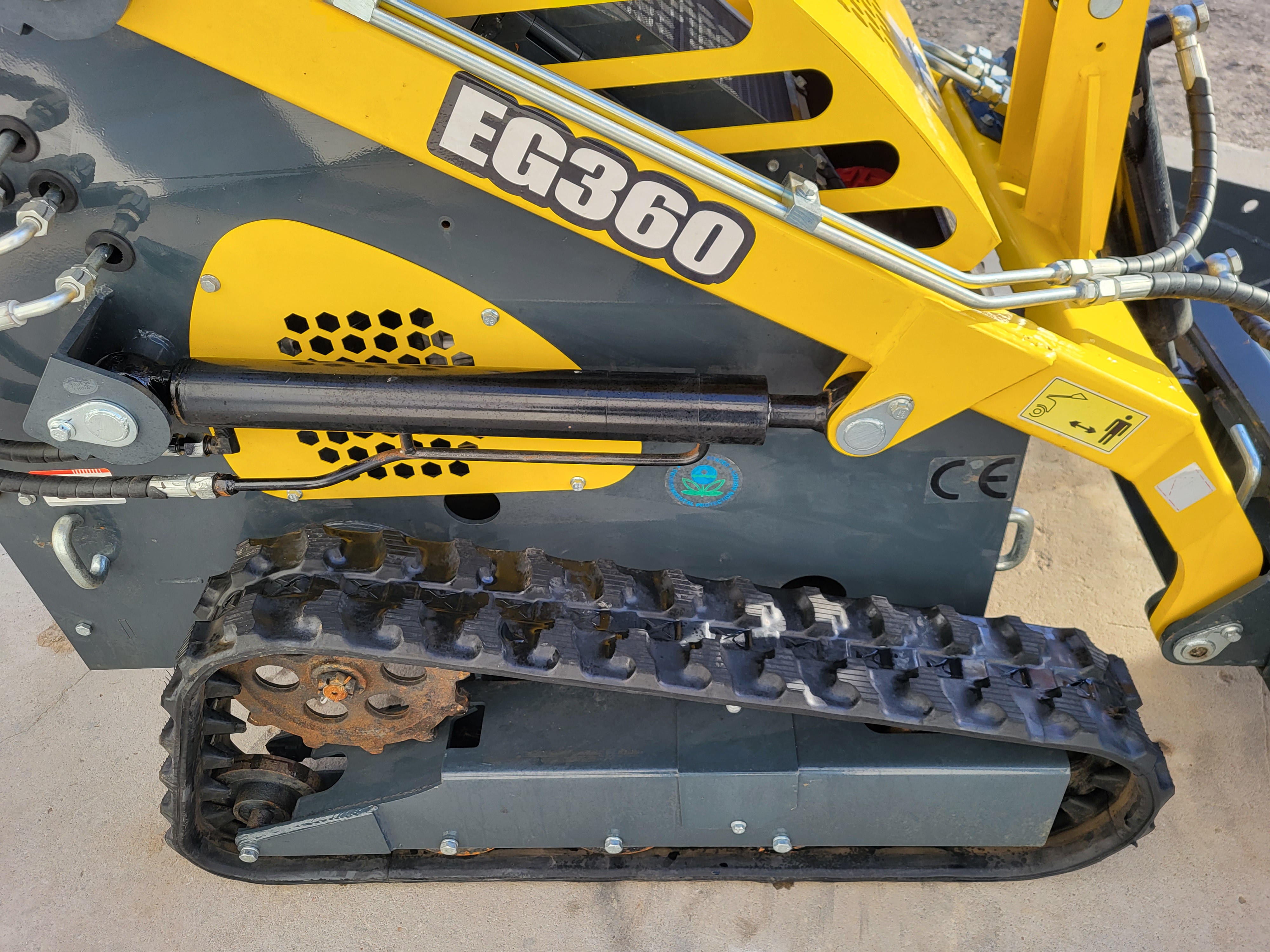 EG360 mini skid steer side: boom with tilt cylinder, vented engine cover and rubber track on a steel drive sprocket