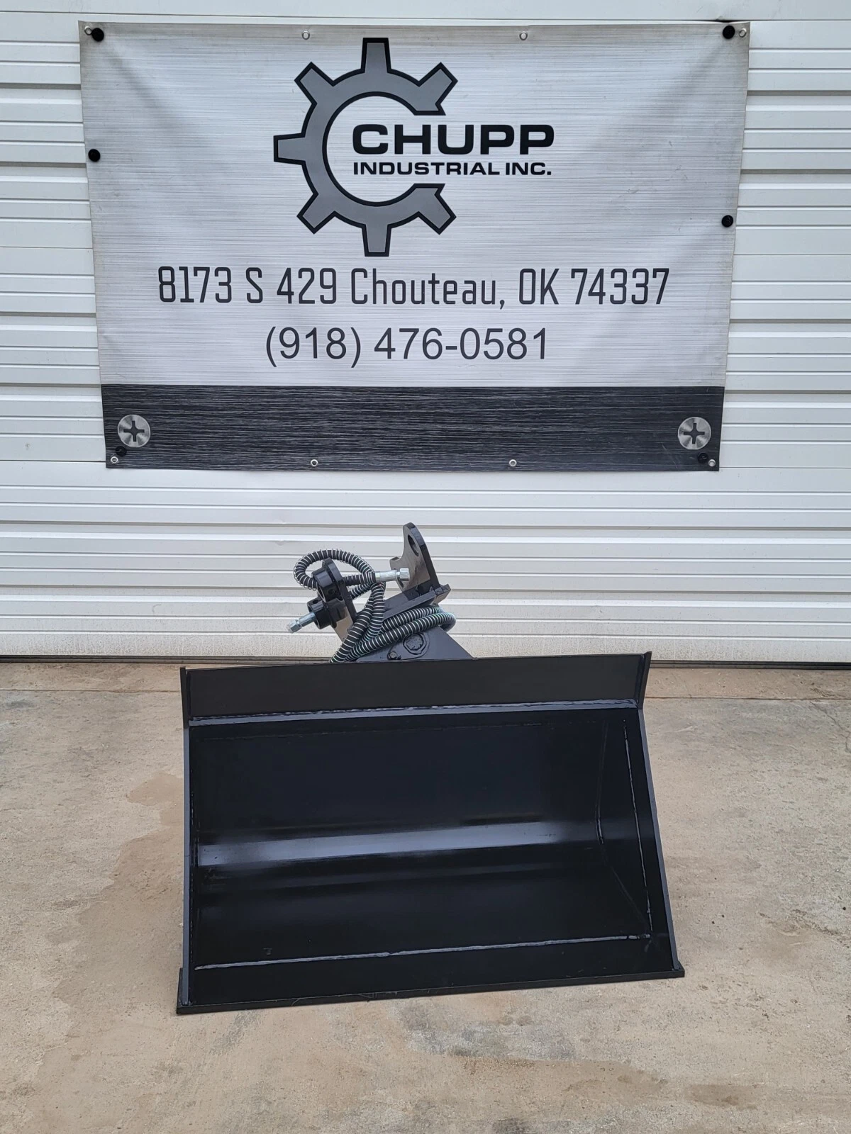 Black hydraulic tilt bucket head-on, wide smooth cutting edge and tilt coupler with coiled hoses
