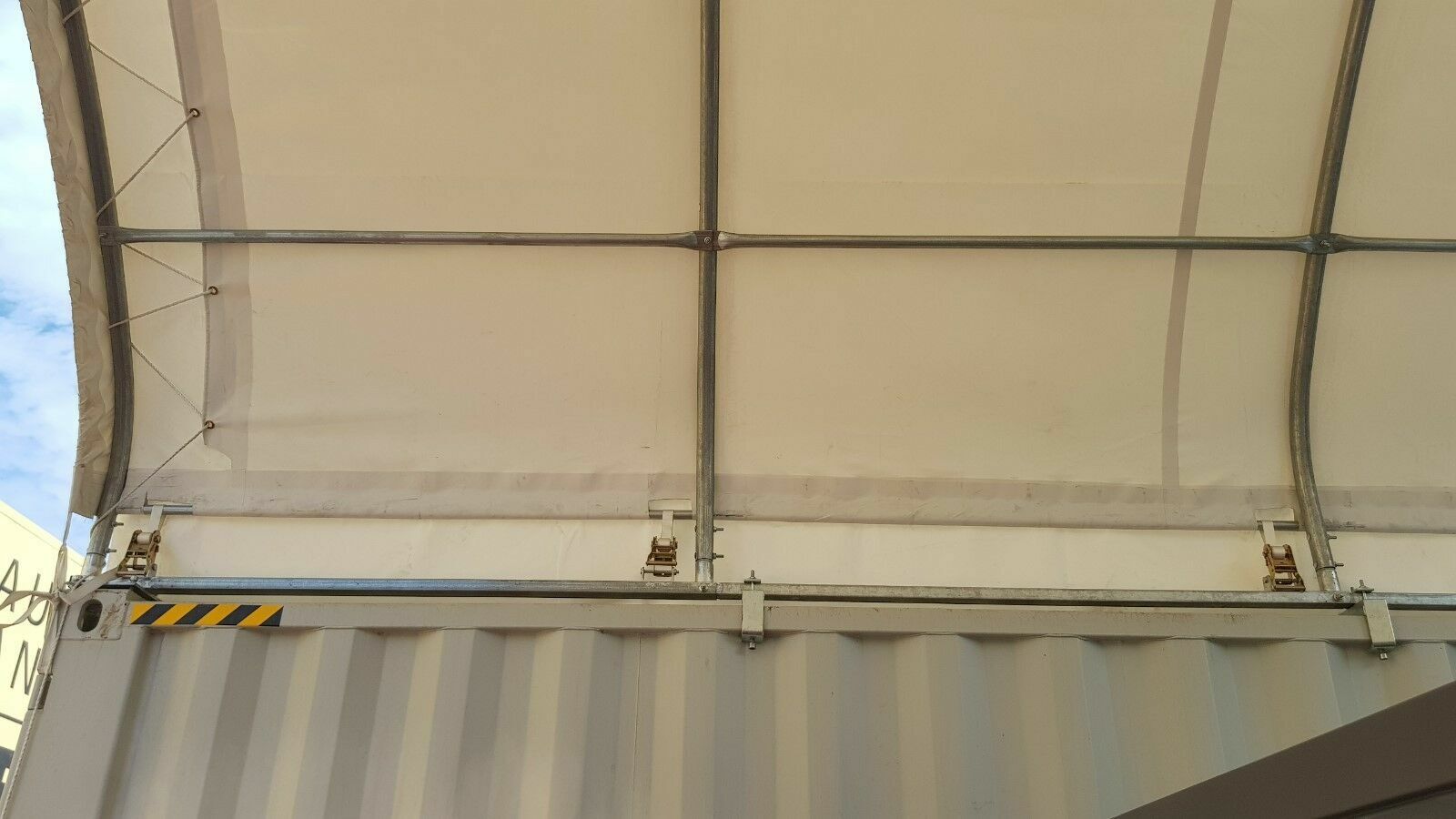Container shelter's white PVC cover from inside, stretched over galvanized arches with ratchet tensioners at the rail