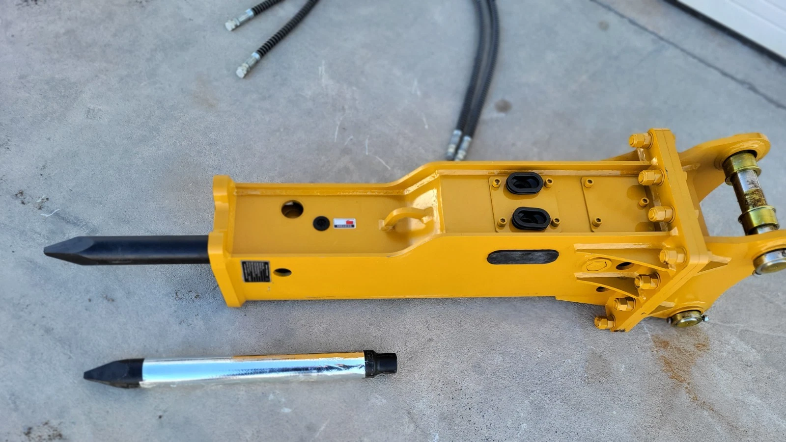 Yellow SB45 hydraulic breaker from above, moil chisel fitted, bracket pins and bushings, spare chisel and hoses