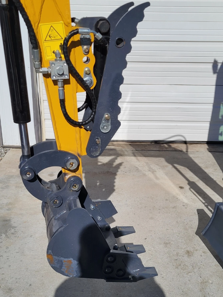 QK18RXS-C digging bucket and toothed hydraulic thumb on the yellow arm, with the hoses that drive them