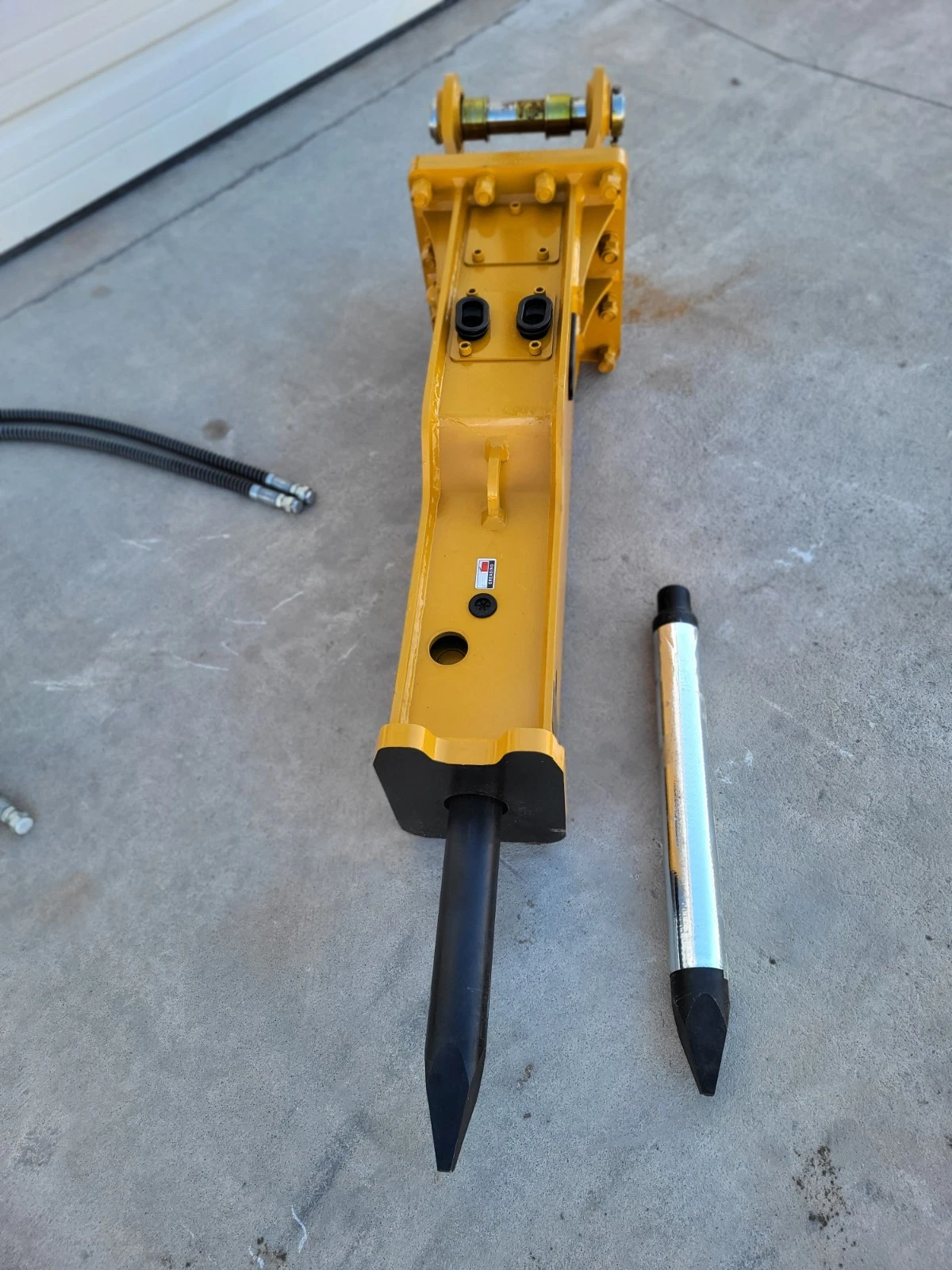 SB45 hydraulic breaker viewed down its length, moil chisel fitted and a spare chrome chisel alongside
