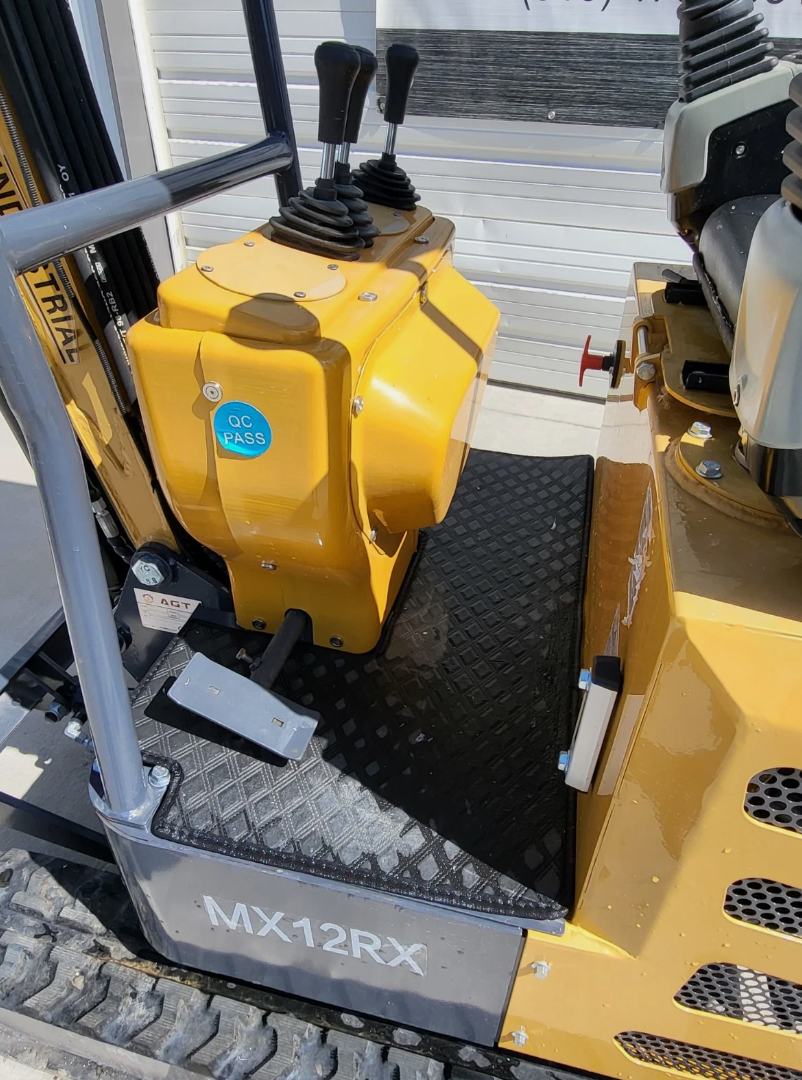 MX12RX mini excavator platform: two booted travel levers, foot pedal, rubber mat and the model decal on the frame