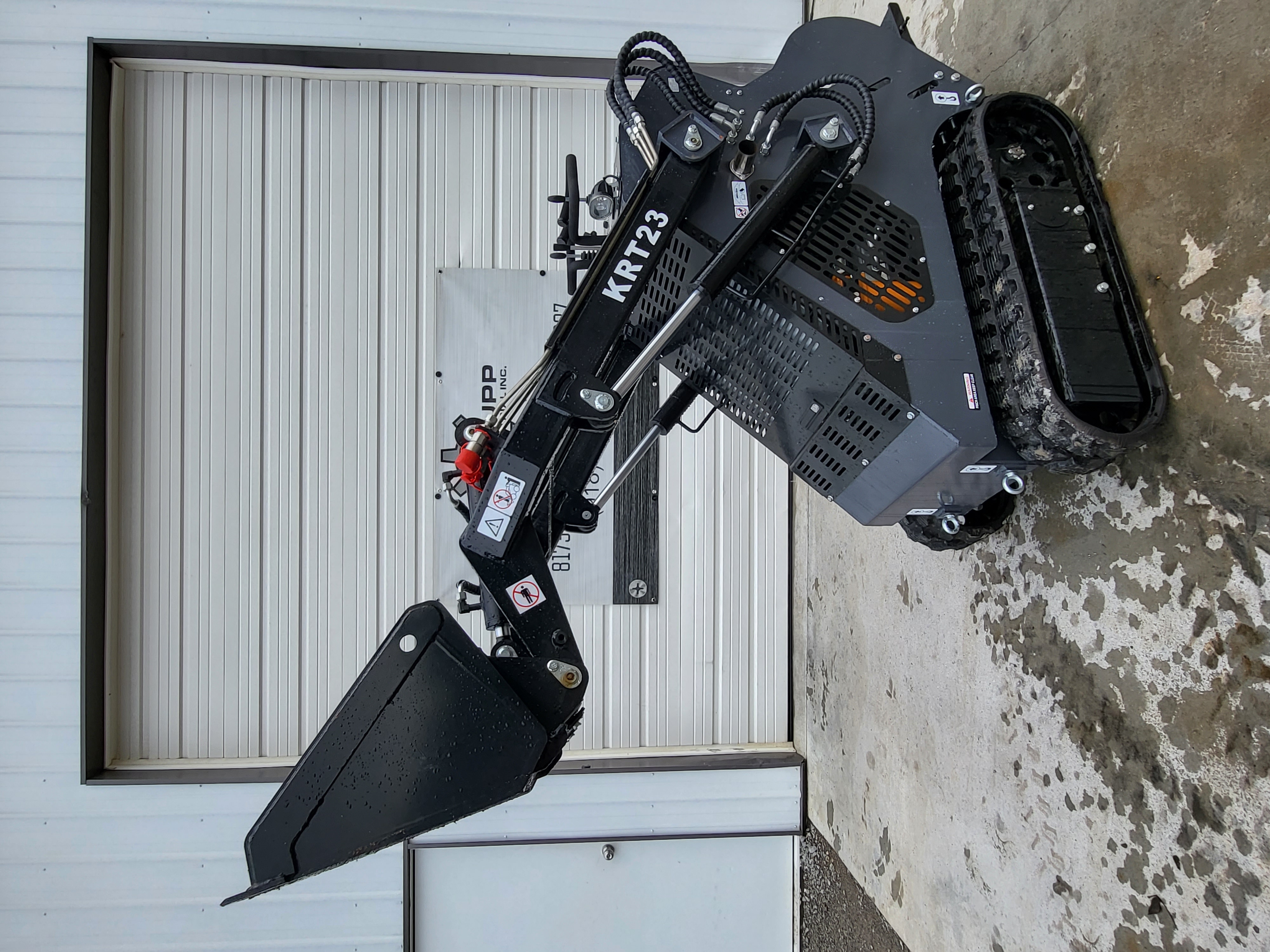 AGT KRT23 mini skid steer with the loader arms out and bucket tilted down, hydraulic hoses and rubber tracks