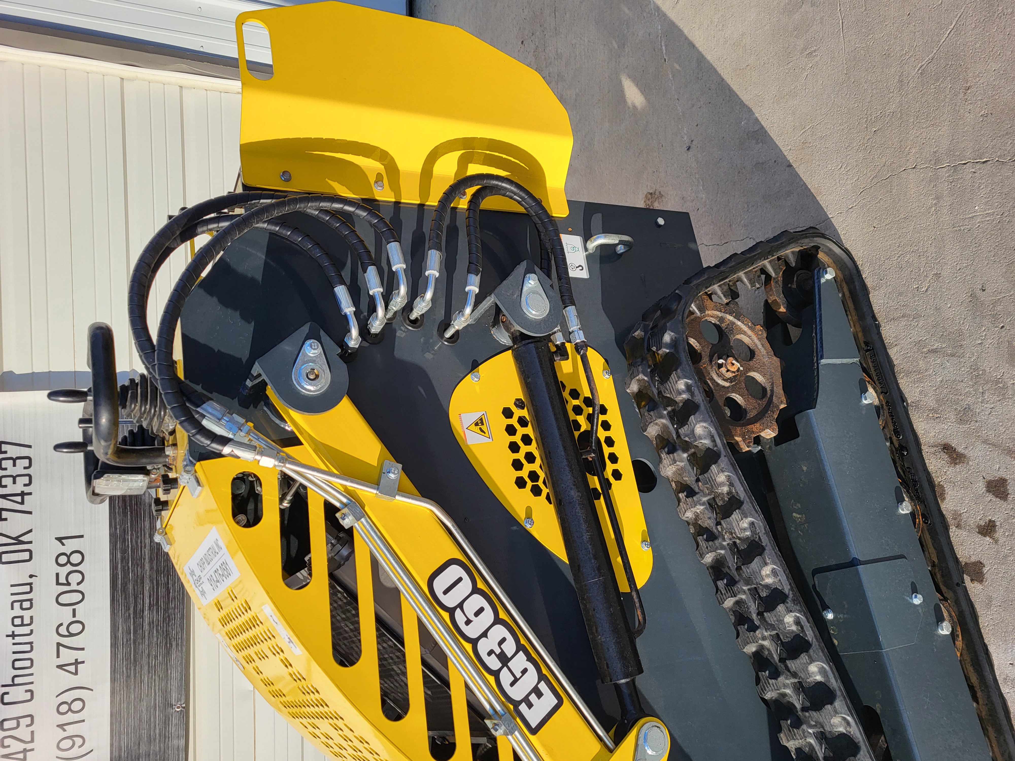 EG360 loader arms: braided hydraulic hoses and lift cylinders over the black boom, rubber tracks and drive sprocket