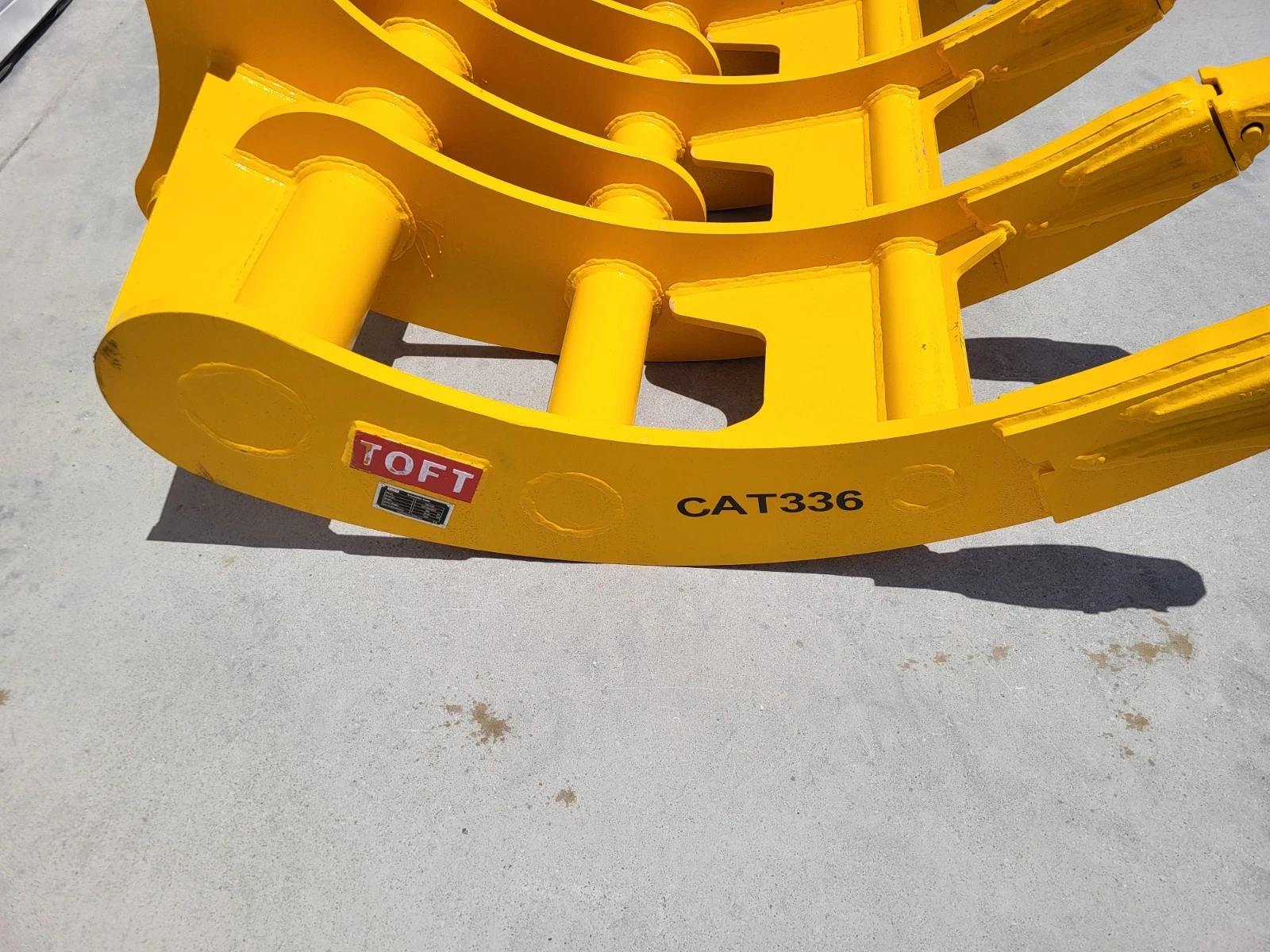 CAT336 marking and red TOFT badge on the edge of the yellow excavator rake, curved tines behind