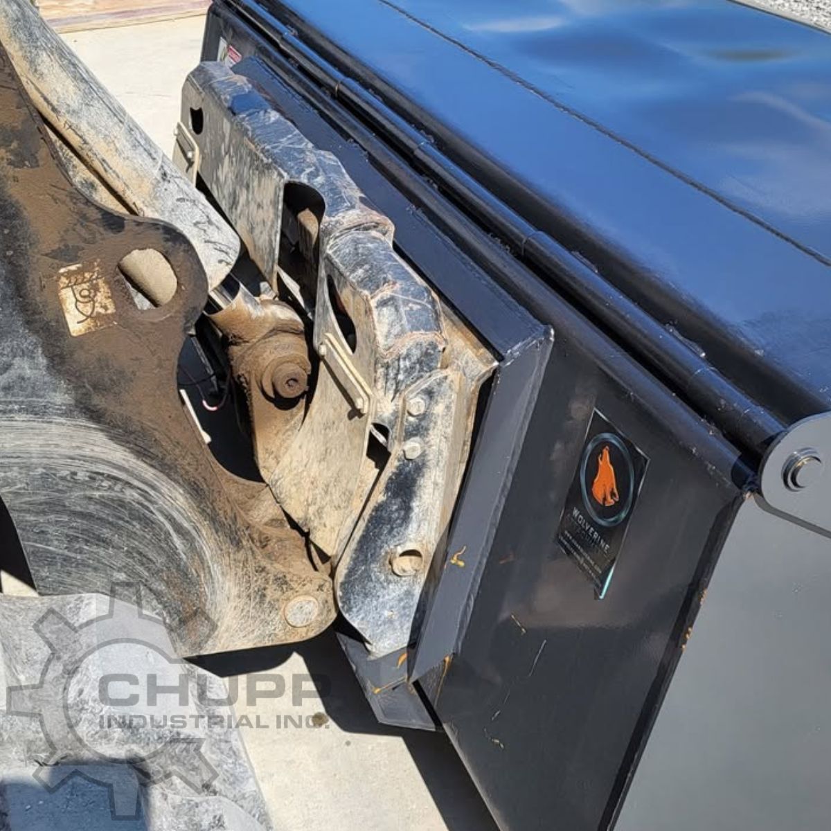 Wolverine box broom coupled to a skid steer quick-attach plate, brand decal on the black hood