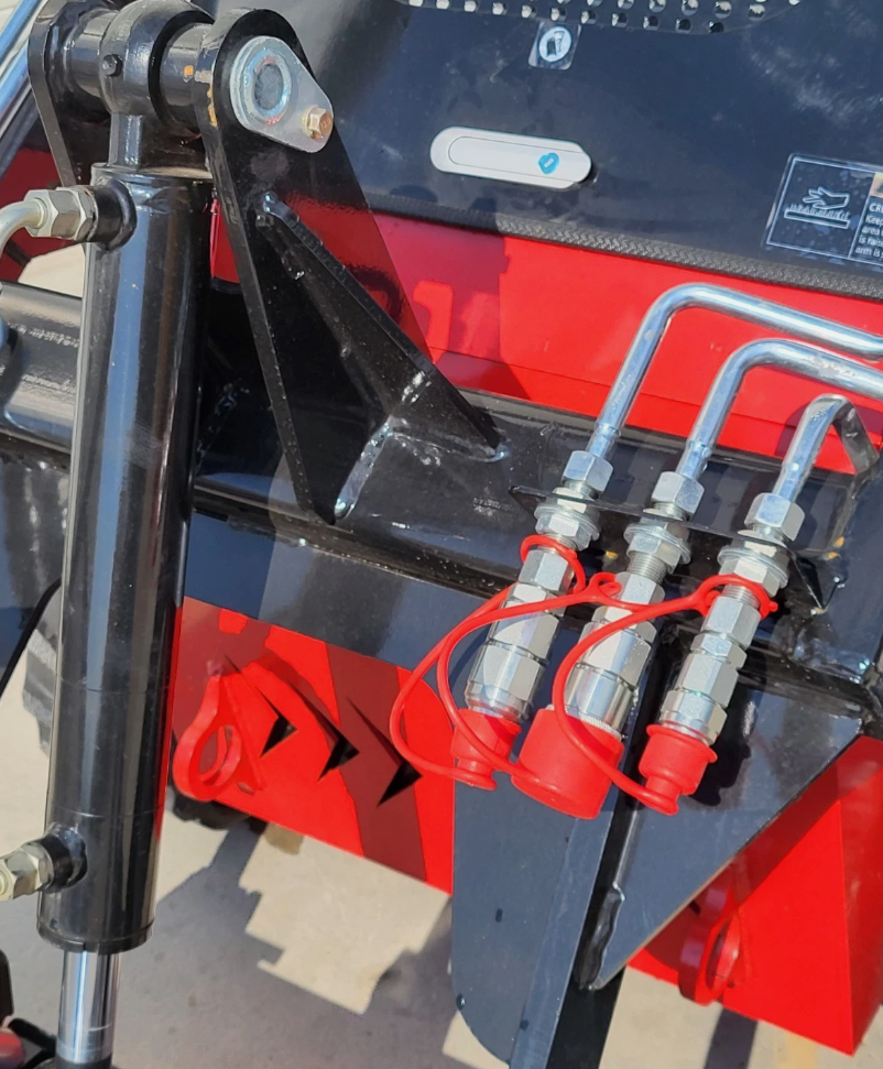 Front quick-attach plate of the red mini skid steer, three hydraulic couplers under red dust caps and a lift cylinder
