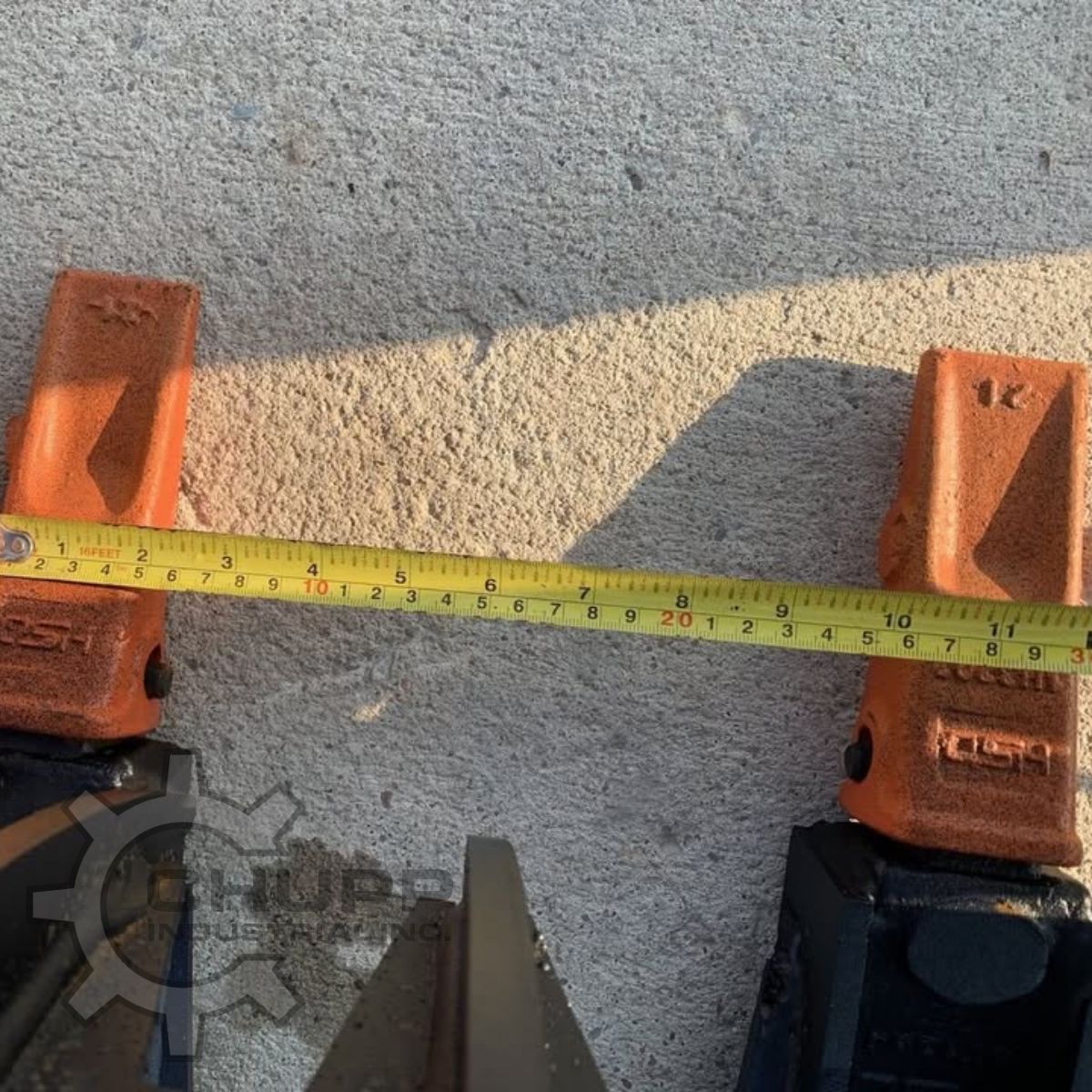 Greatbear grapple rake tooth spacing measured with a tape between two orange bolt-on cast teeth