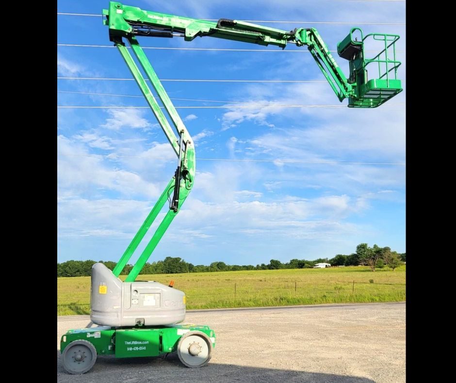 Green articulating boom lift, boom raised and reaching out sideways with the empty work platform at the end