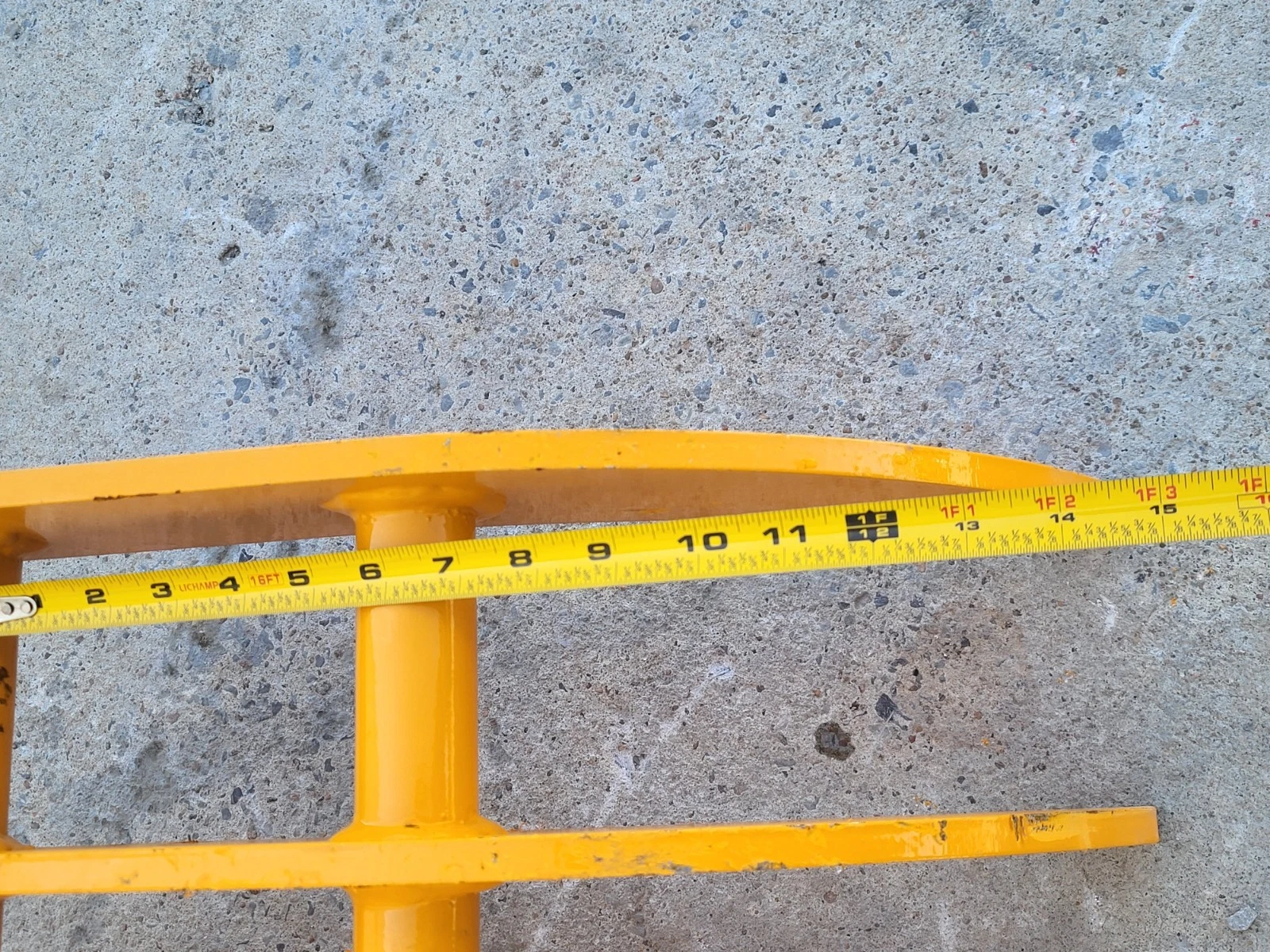 Tape measure laid along the yellow rake's curved tine, scale running past 15 inches