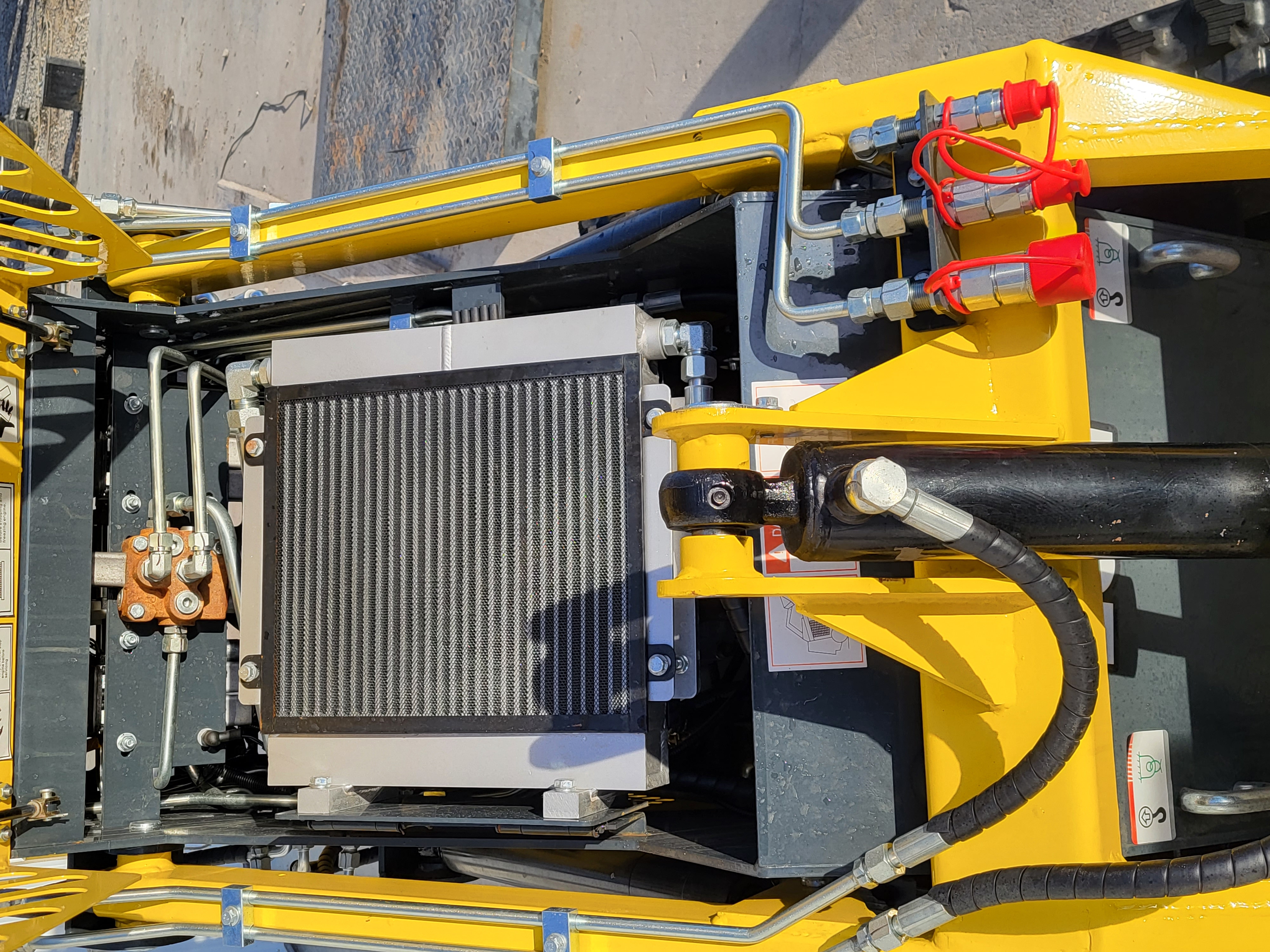 EG360 hydraulic oil cooler mounted in the frame, with red-capped auxiliary couplers and the lift cylinder alongside