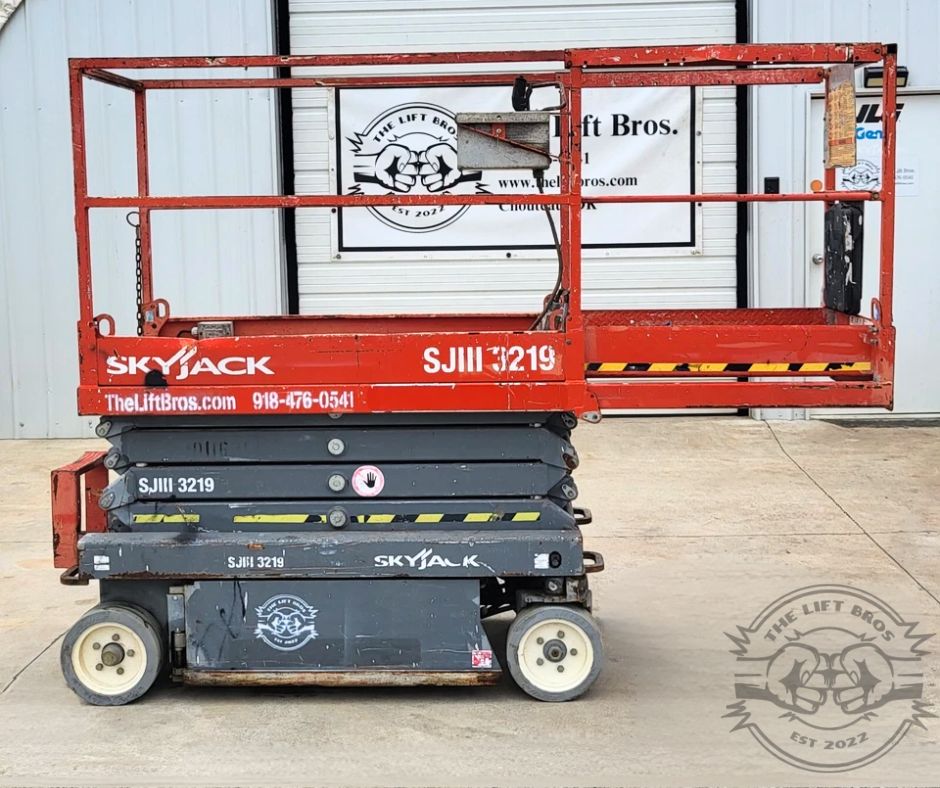 Red Skyjack SJIII 3219 scissor lift, side view fully lowered, guardrails around the platform and non-marking wheels