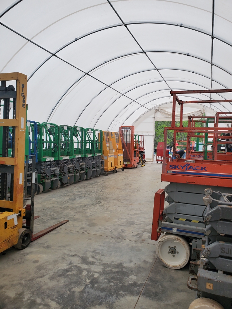 Fabric building interior: white PVC cover on arched steel ribs, clear span over concrete floor lined with stored lifts