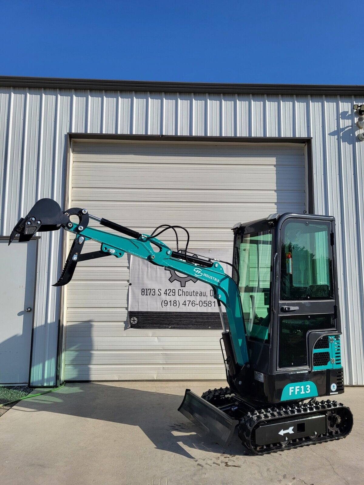 FF13 mini excavator with the teal arm stretched out, hydraulic thumb and bucket raised, dozer blade on the ground