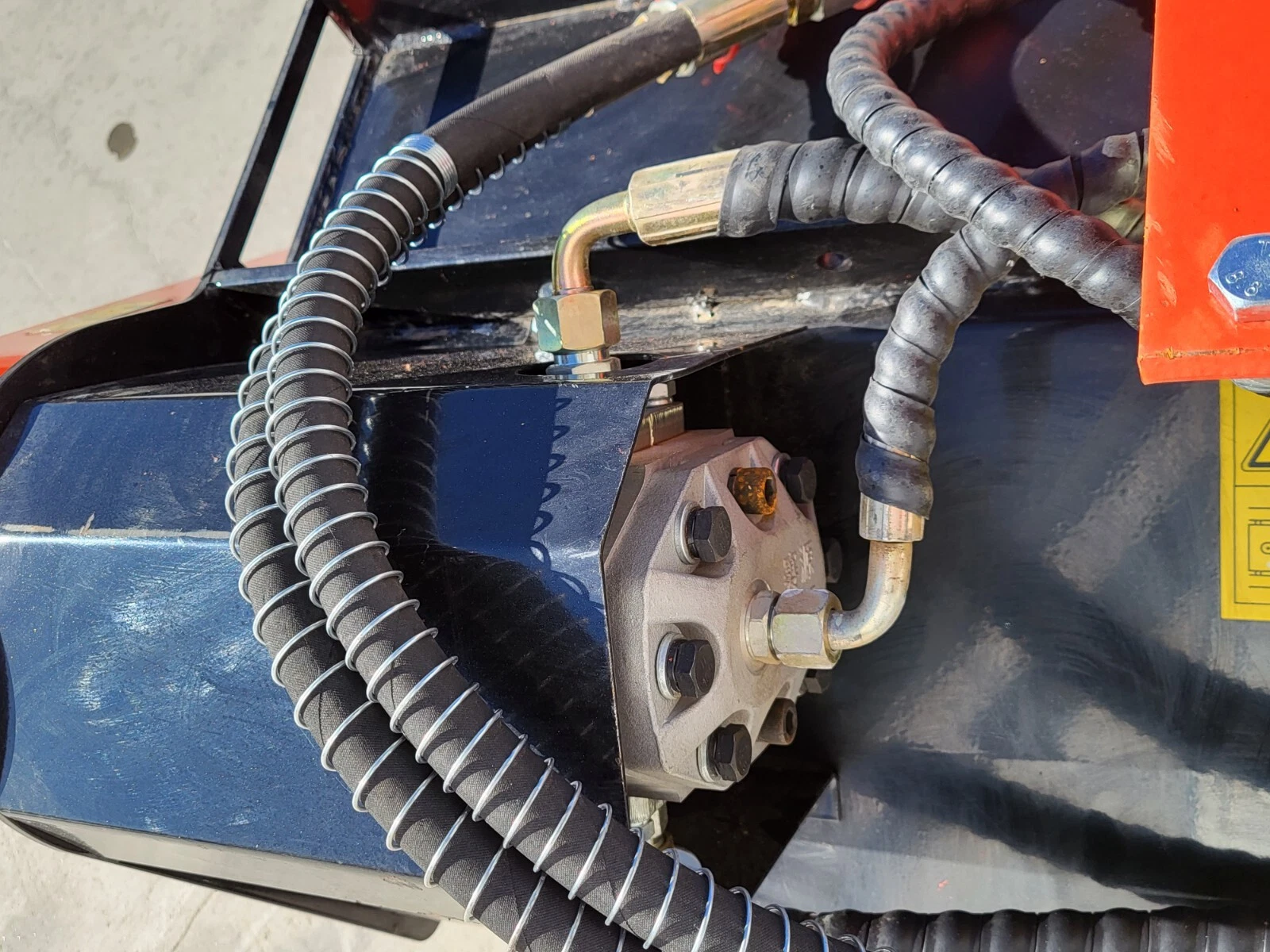 Flail mower's hydraulic drive motor bolted to the deck, sheathed hoses and elbow fittings running to it
