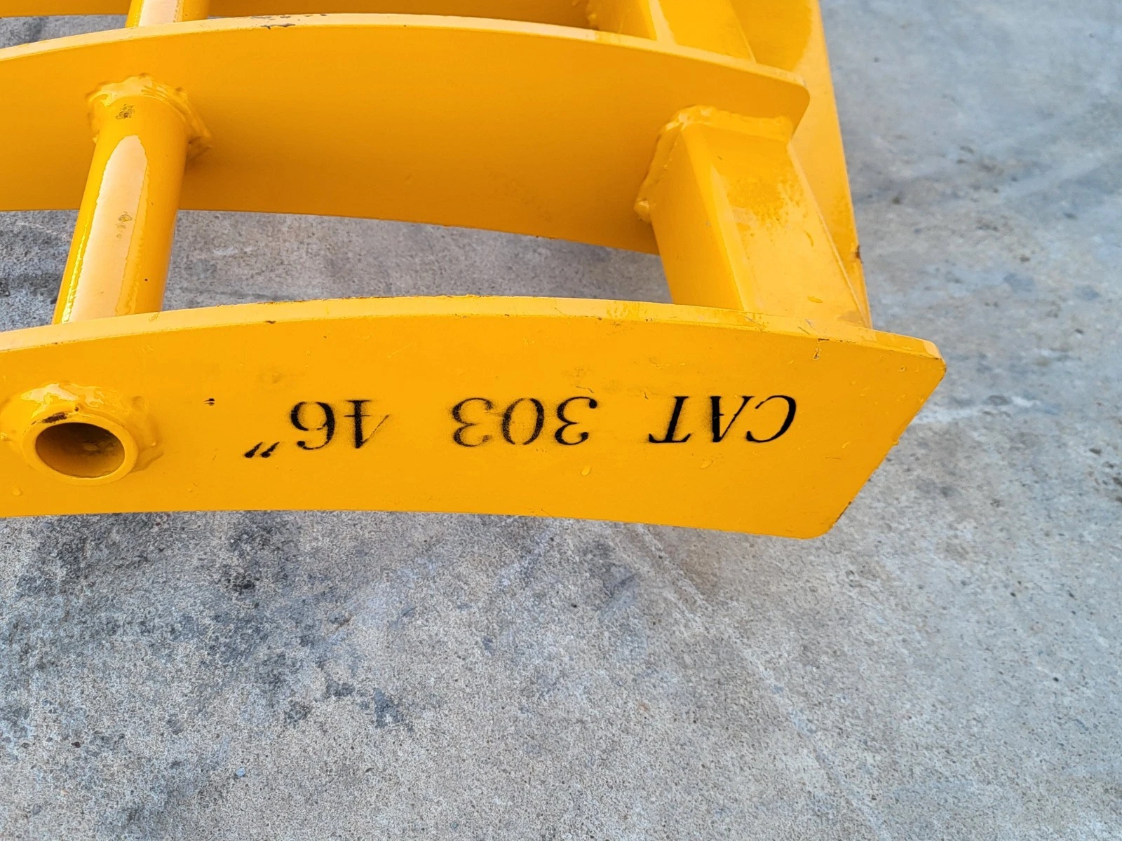 Yellow rake's outer tine bar stamped CAT 303 46 inch, tubular cross-brace and tine socket alongside