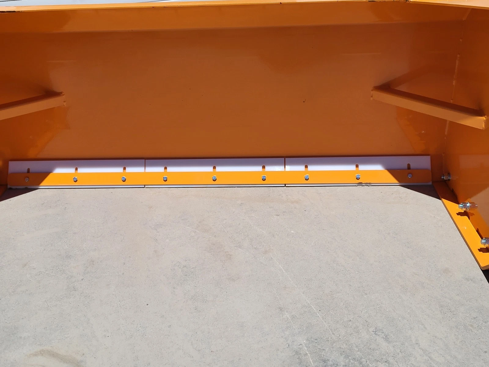 White poly cutting edge bolted across the base of the orange snow blade