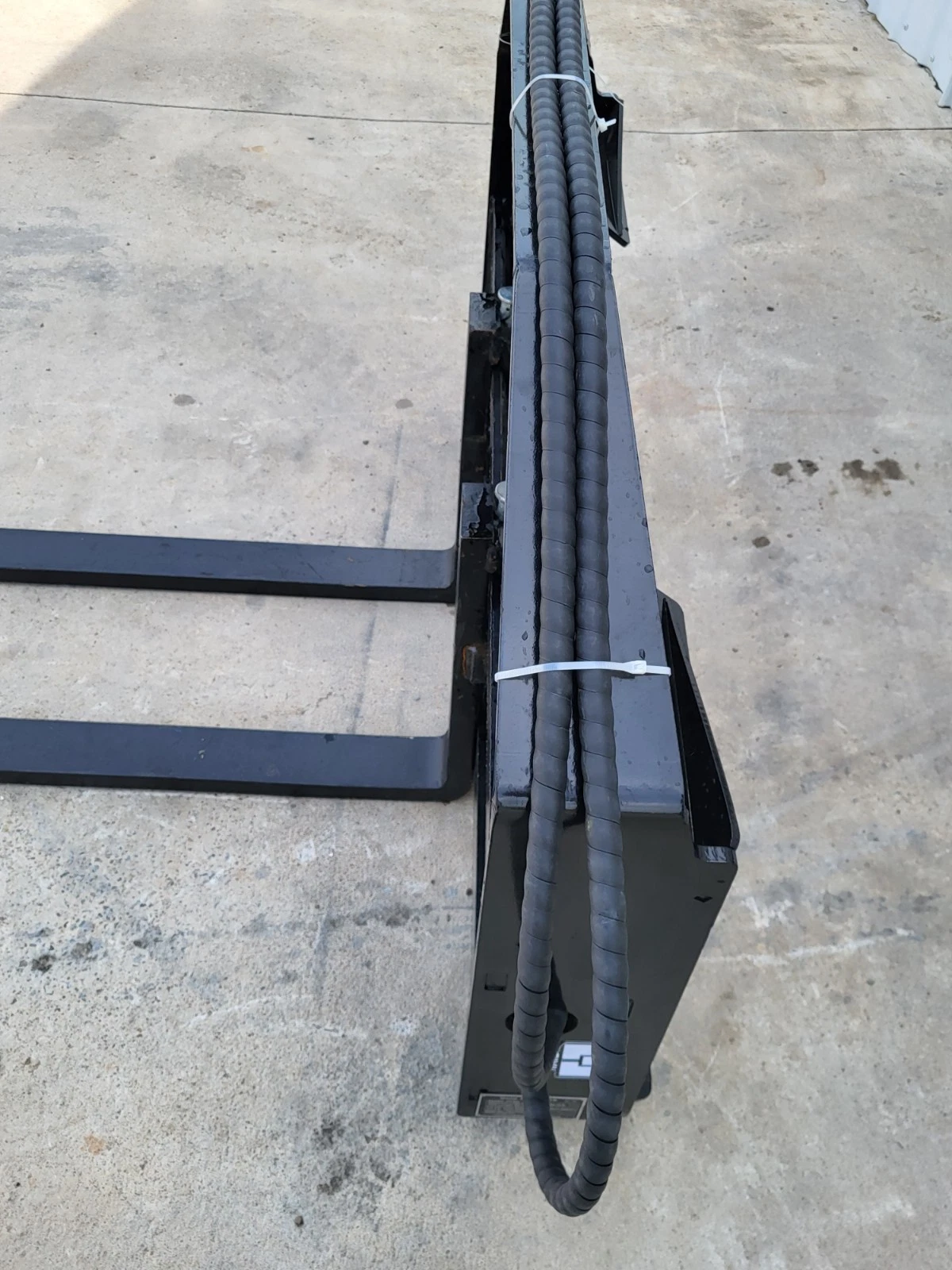 Pallet fork carriage top rail with the sleeved hydraulic hose run zip-tied along it, forks at left