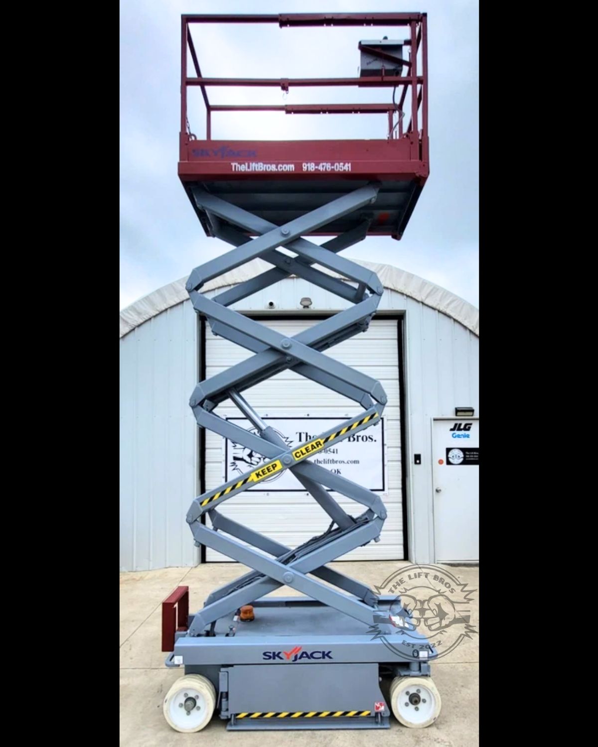 Skyjack scissor lift fully extended, maroon guardrail platform raised on a gray scissor stack