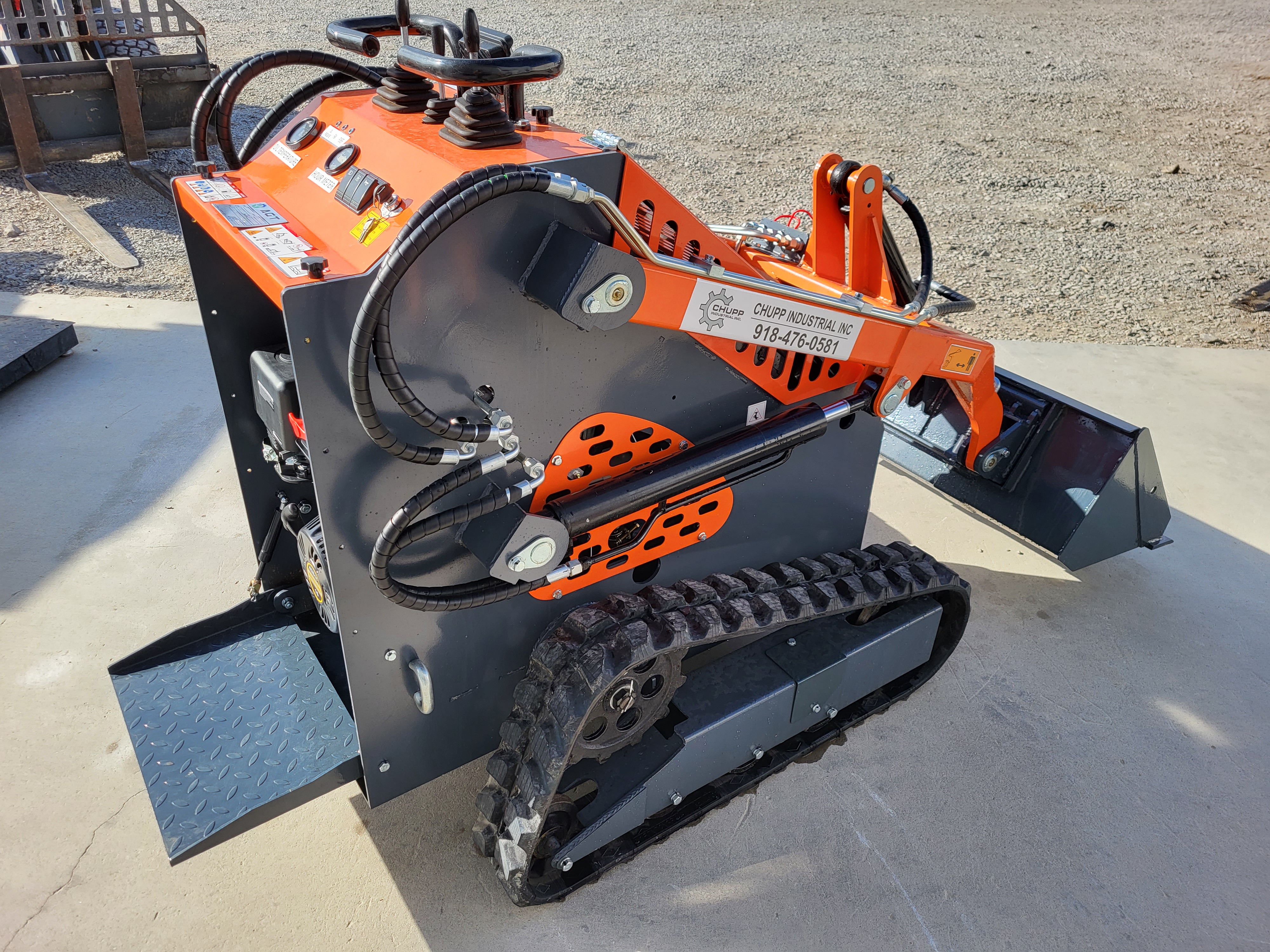 AGT YSRT14 mini skid steer from the rear, gray bucket tilted forward, rubber tracks and fold-down stand-on platform