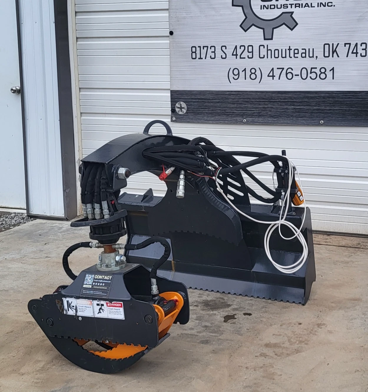 Rotating grapple with an orange serrated jaw on a hydraulic rotator, boom arm and coiled hoses