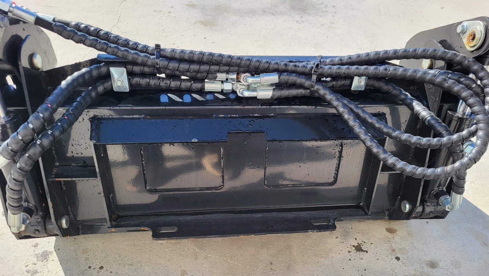 Rear of the 4-in-1 bucket: quick-attach mount plate with braided hoses and steel fittings running across it