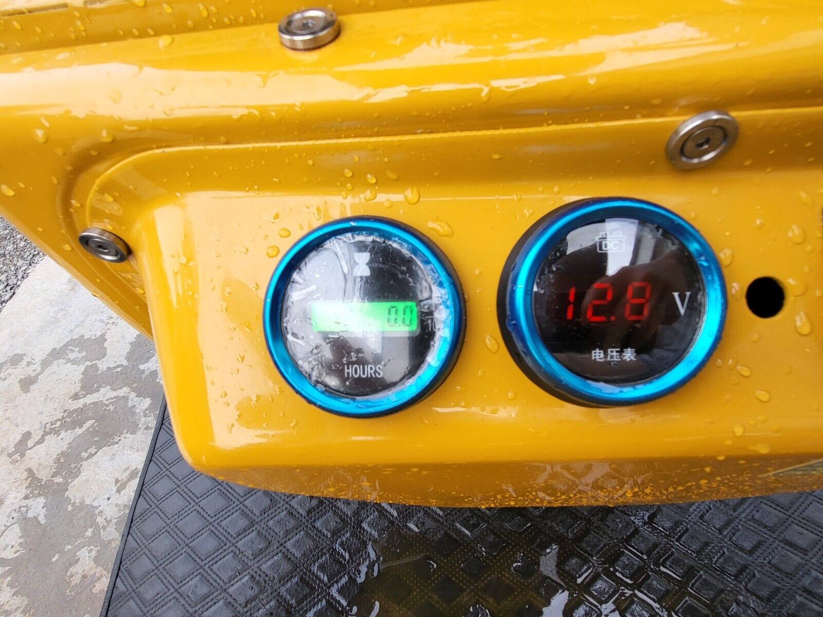 DM12-C gauges: hour meter reading 0.0 hours next to a DC voltmeter showing 12.8 volts, blue bezels on the yellow console