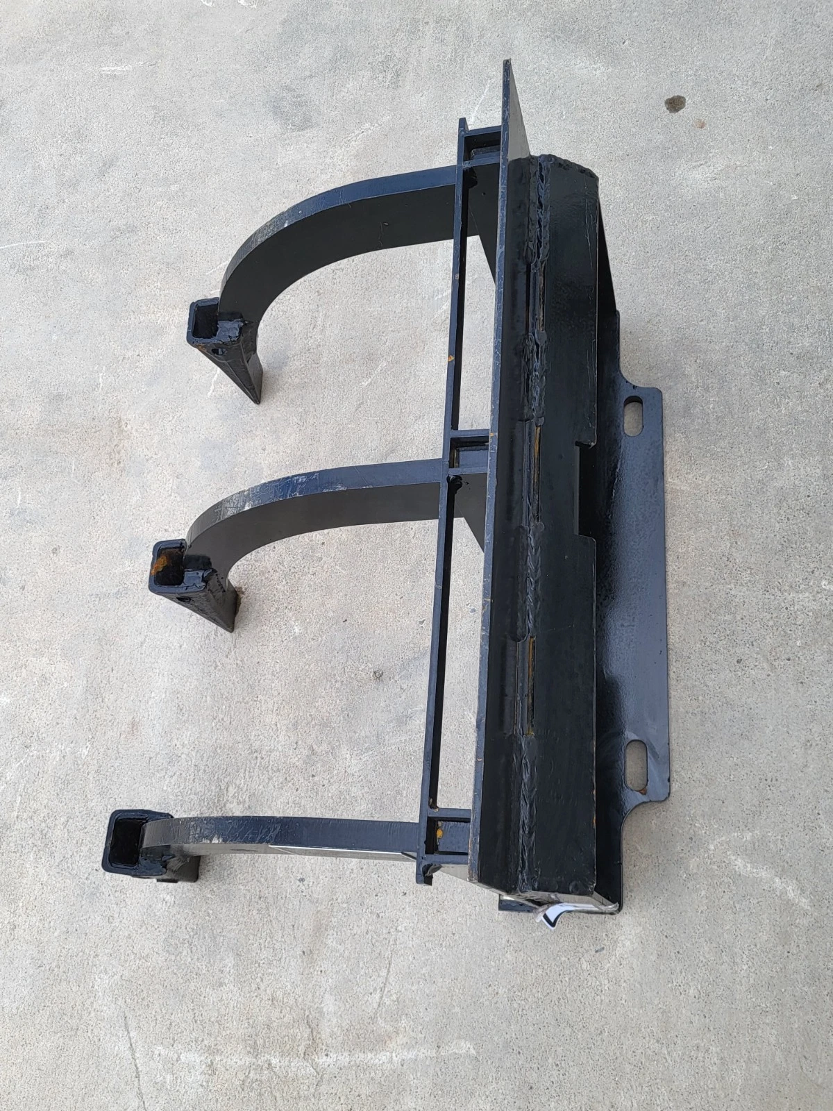 Ripper from the side: quick-attach mount plate with mounting slots and three curved shanks with boot tips