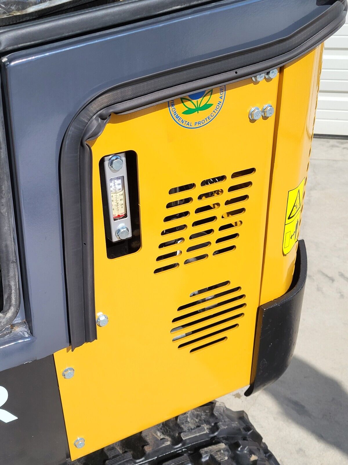 AGT H13R hydraulic sight gauge on the vented yellow side panel, beside the cab door seal and EPA decal